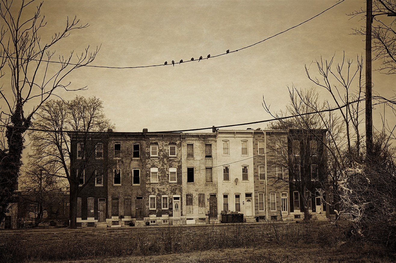 Old brick building with multiple windows, trees on both sides, and a cloudy sky above.