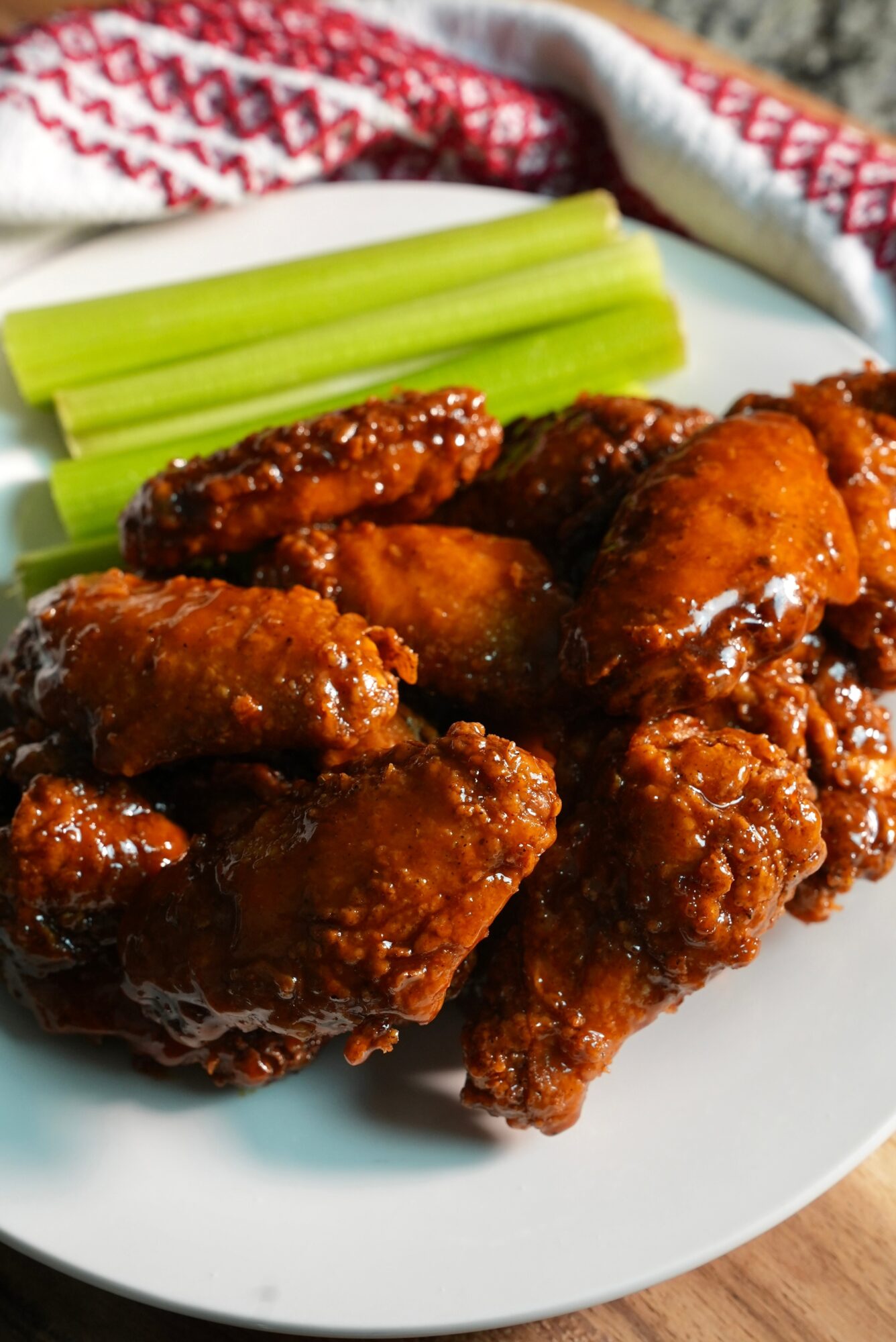 Fried chicken wings with celery sticks on a white plate, with a red and white cloth in the background.