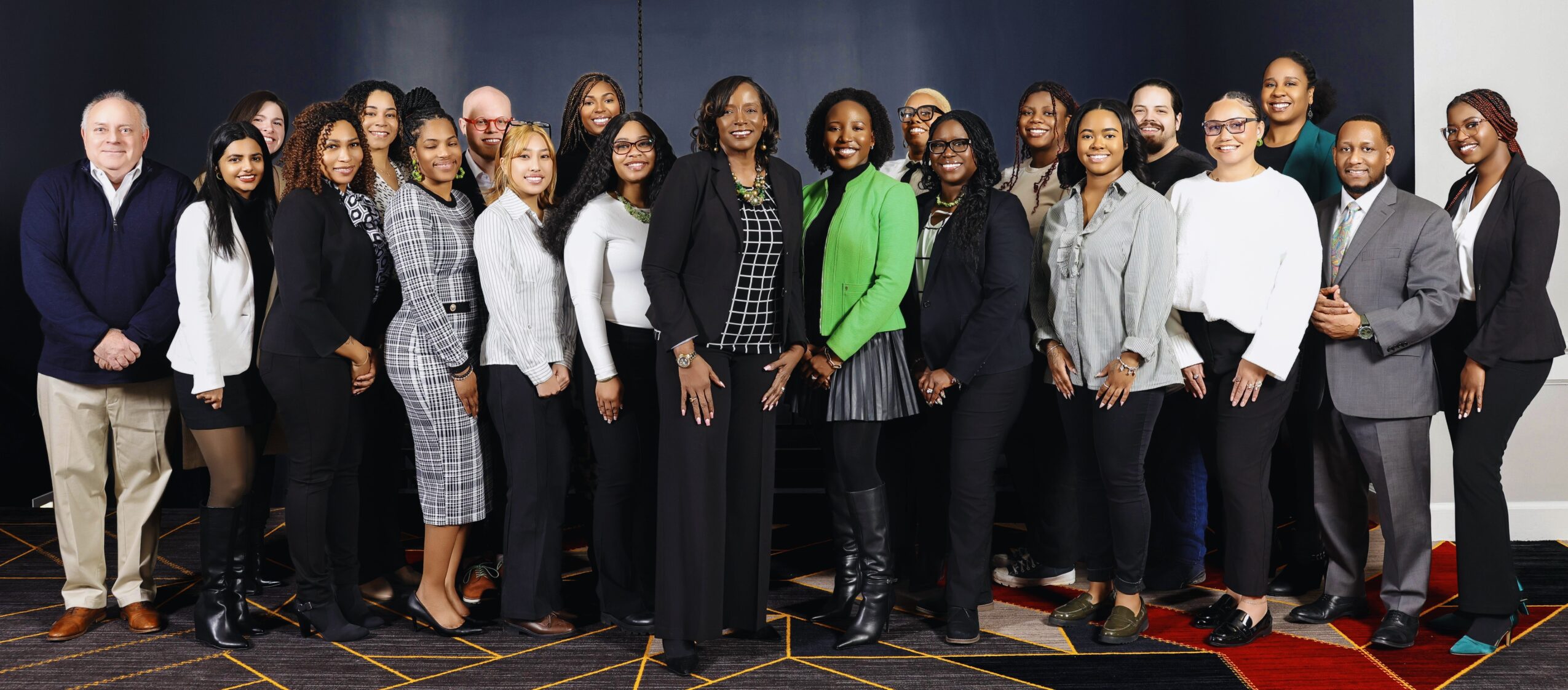 Group of diverse professionals standing together in a conference room, smiling, with a dark background.