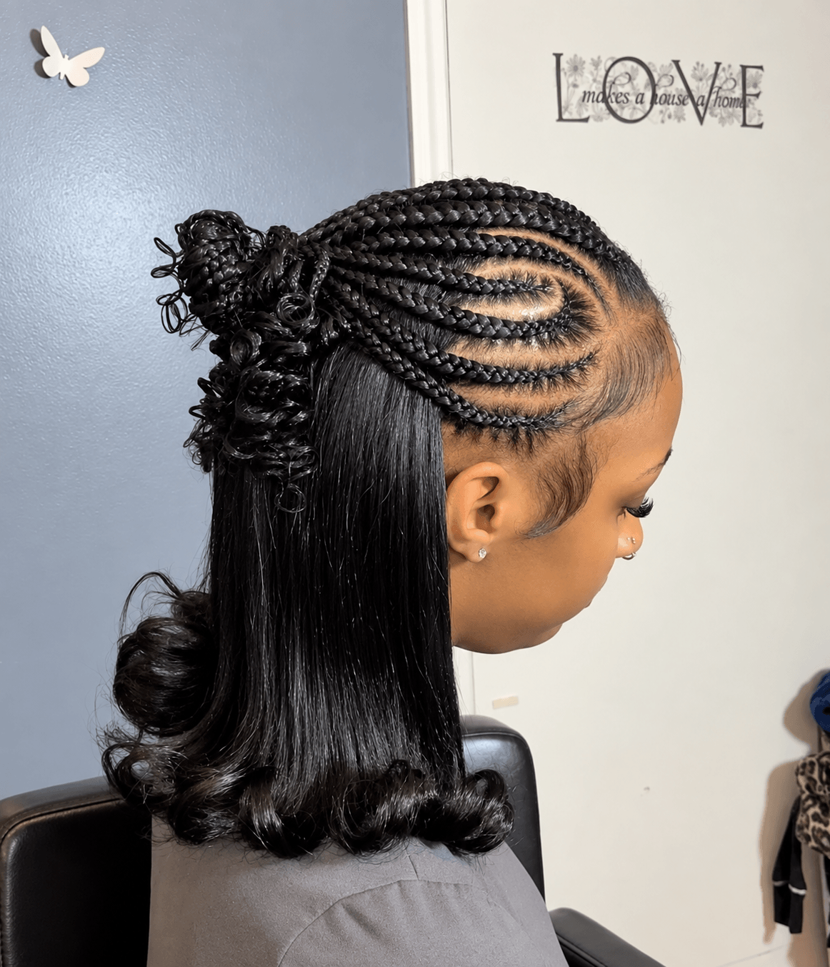 Side view of a woman with braided hairstyle and loose curled hair at the ends, standing indoors near a wall with a 'LOVE' sign.