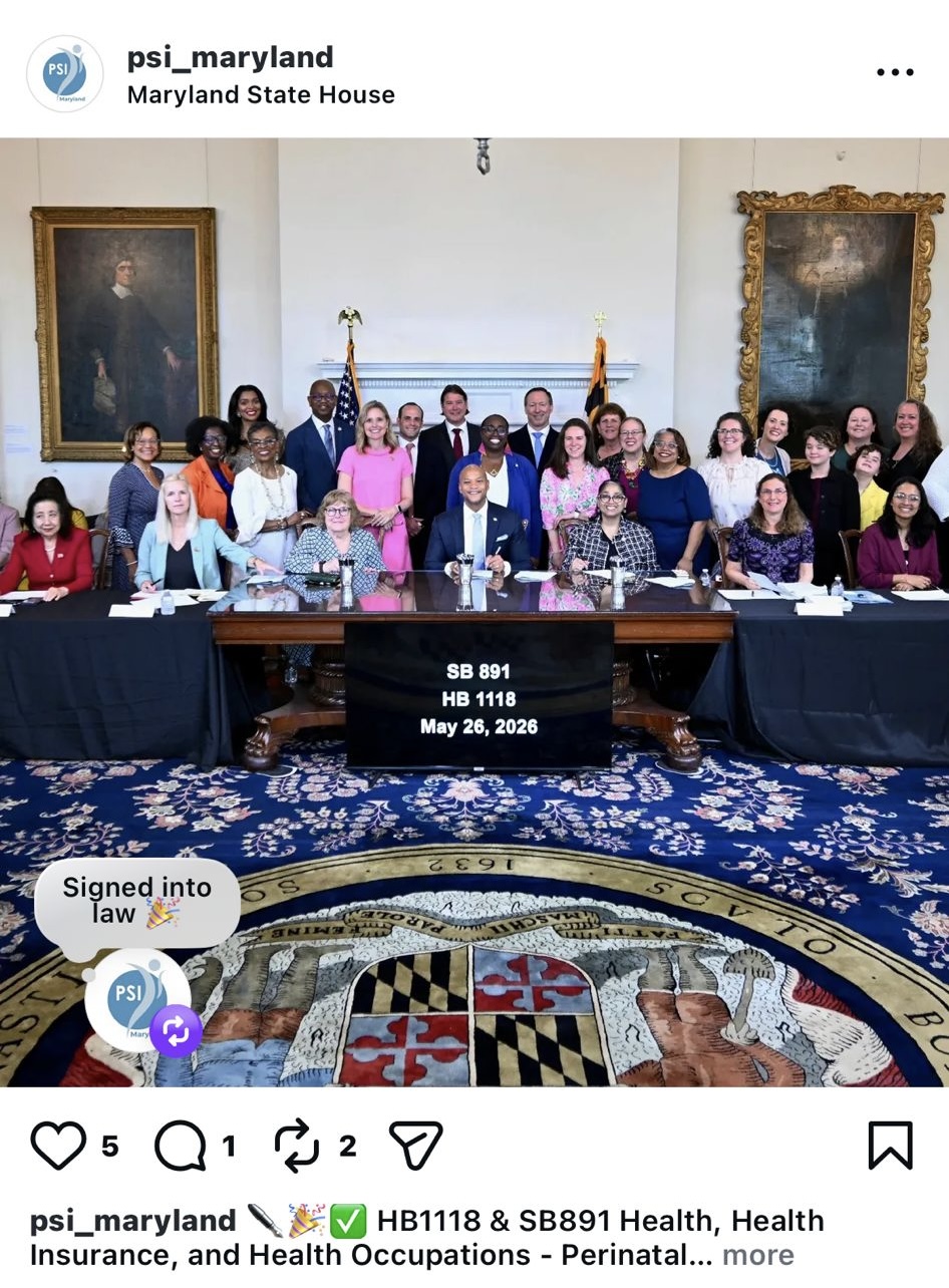 Group of people seated and standing around a table in a room with portraits and a Maryland state seal on the floor.