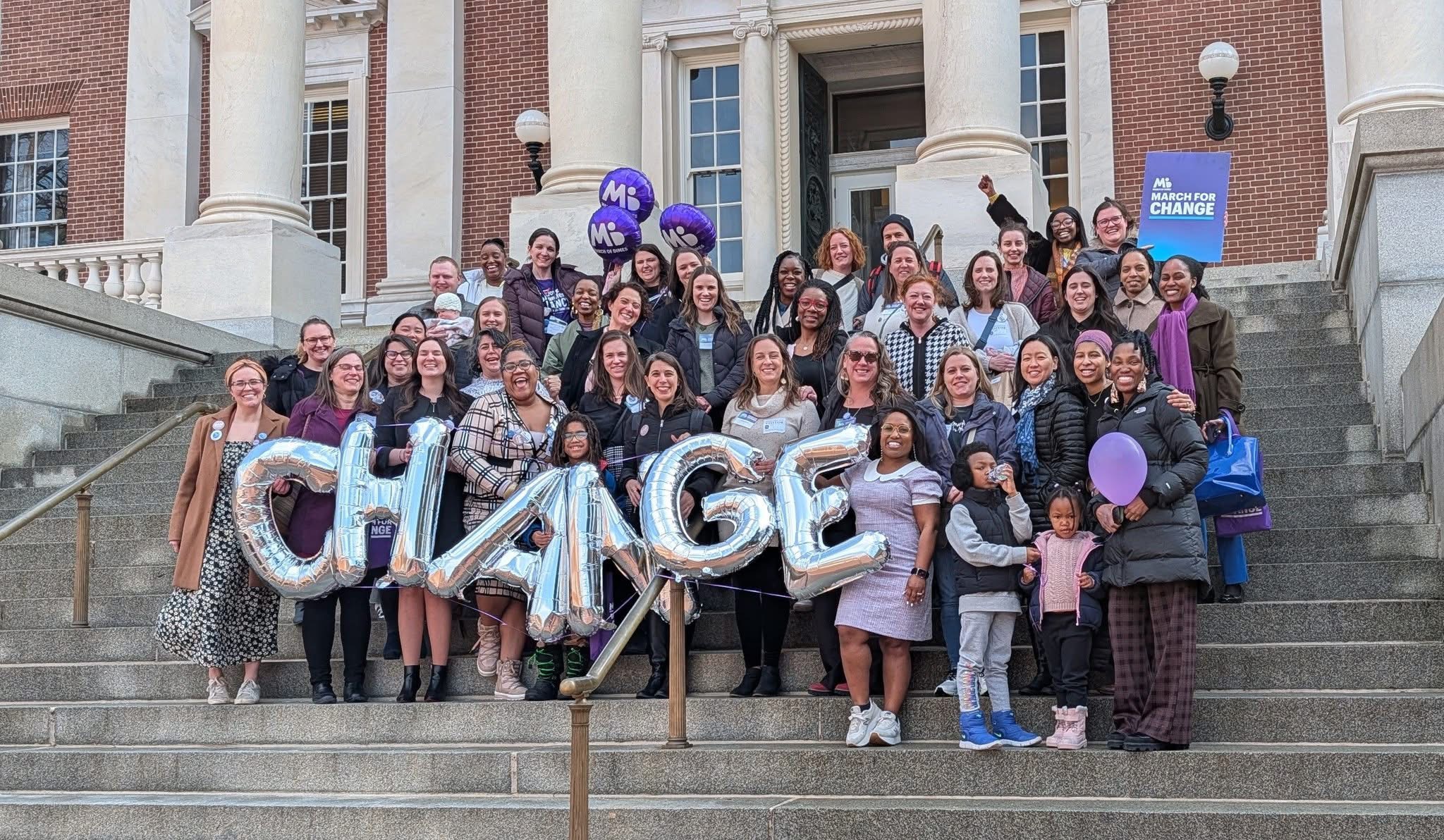 Group of people on stairs holding balloons and large 'CHANGE' sign outside building.