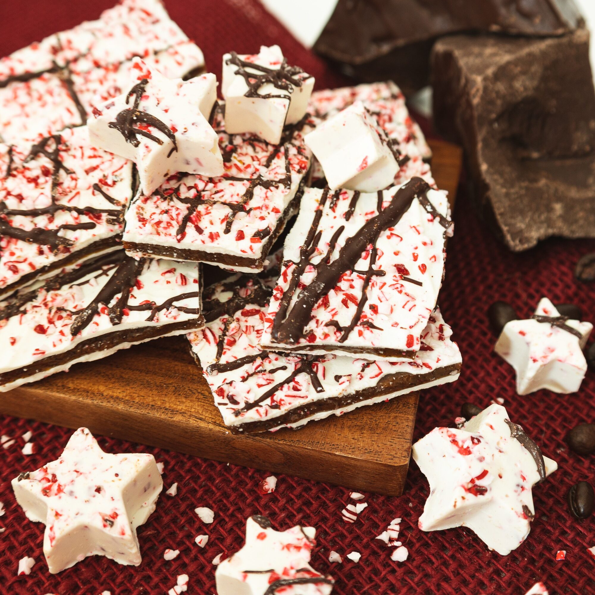 White chocolate bark pieces with red sprinkles and dark chocolate drizzle on a wooden board, beside chocolate chunks.