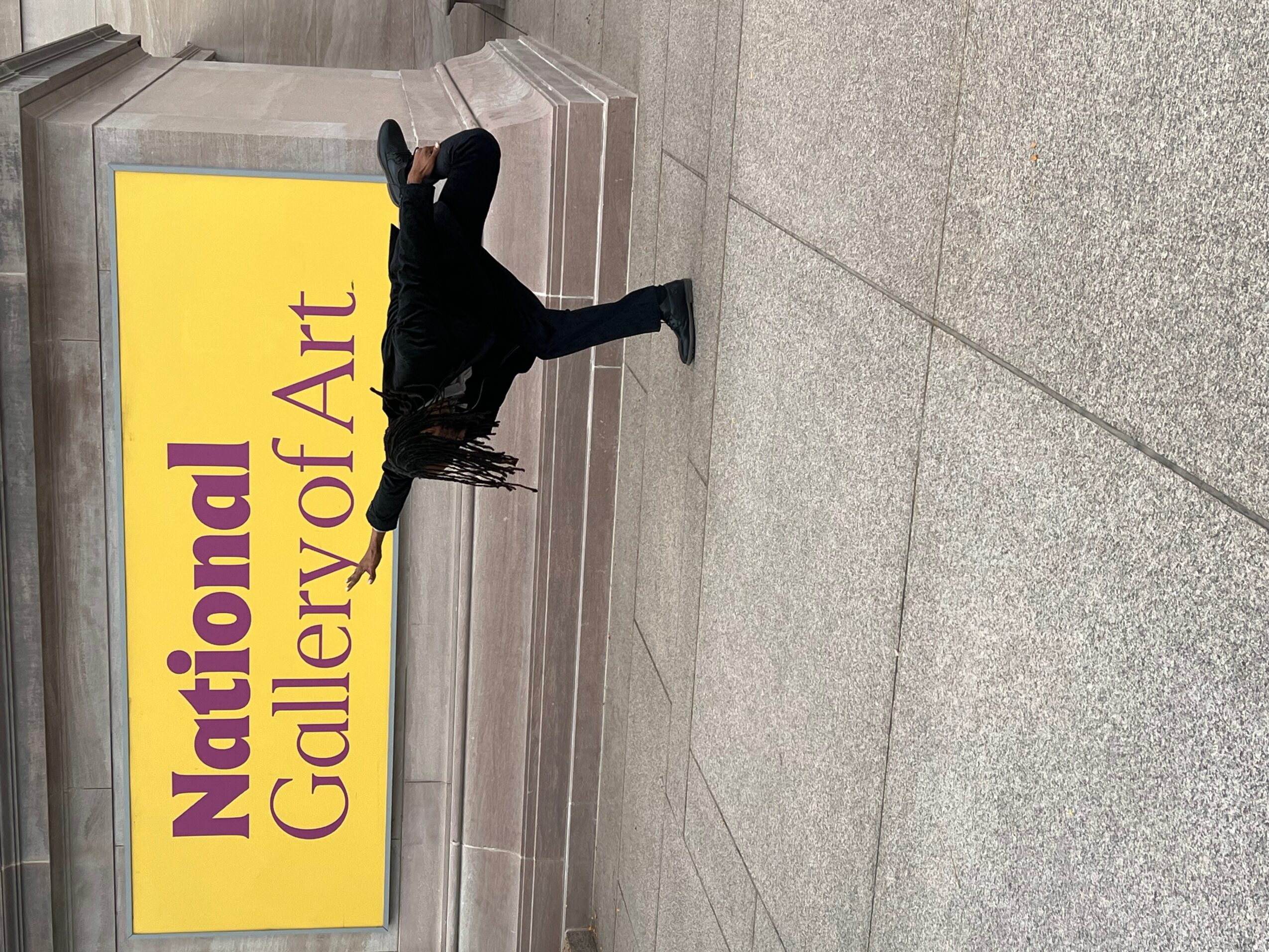 Person walking past a yellow sign that reads 'National Gallery of Art'.