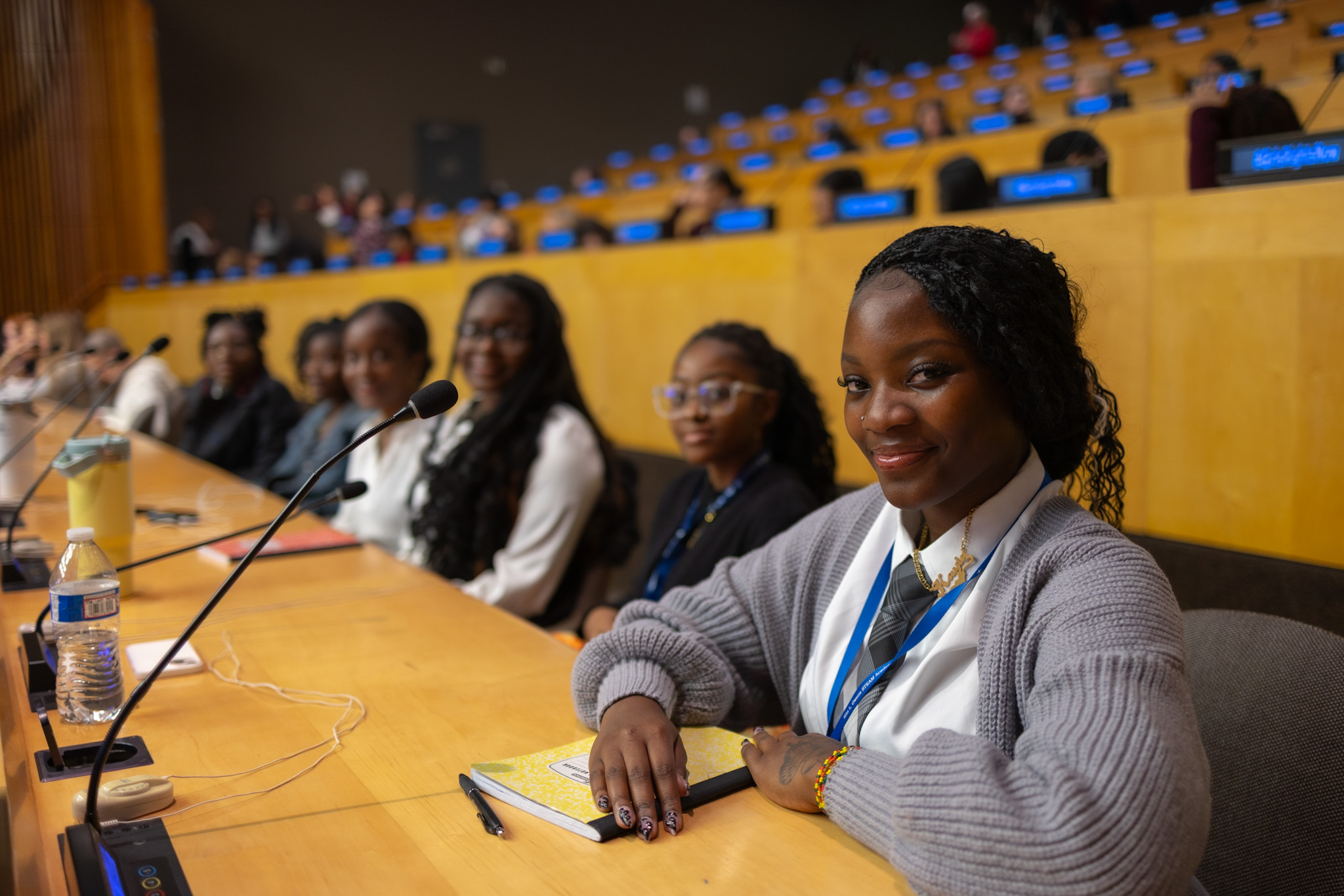 Group of women sitting at a conference table with microphones, some smiling, in a large auditorium.