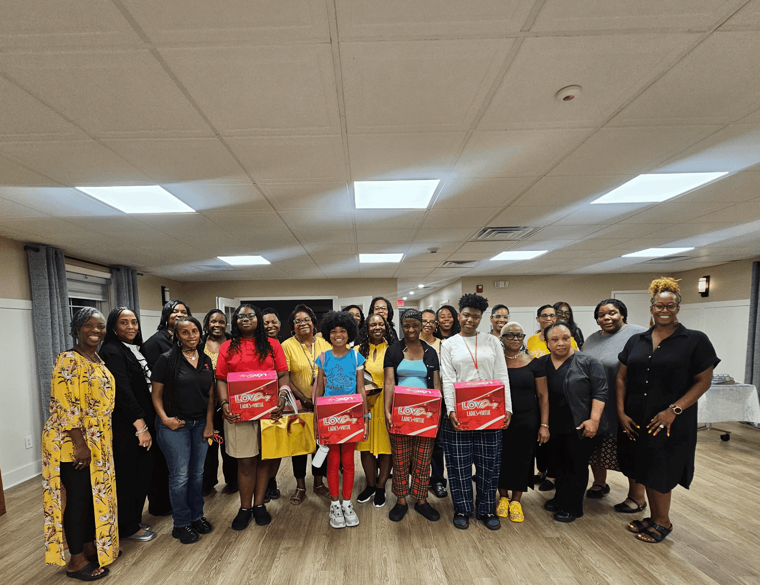 Group of women standing together in a room, some holding red bags, smiling for the photo.