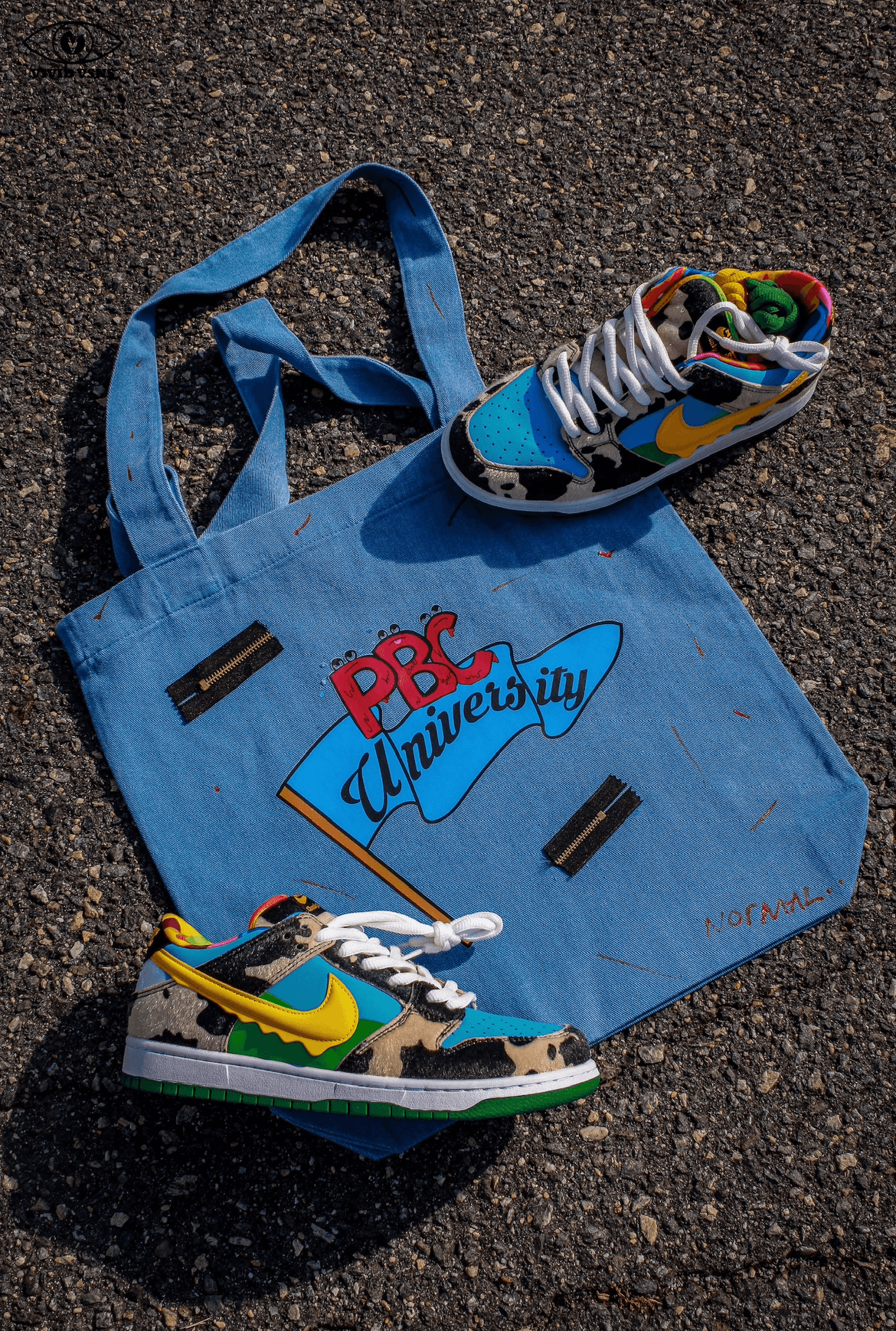 Blue bag with colorful logo, two sneakers with vibrant designs, on asphalt surface.