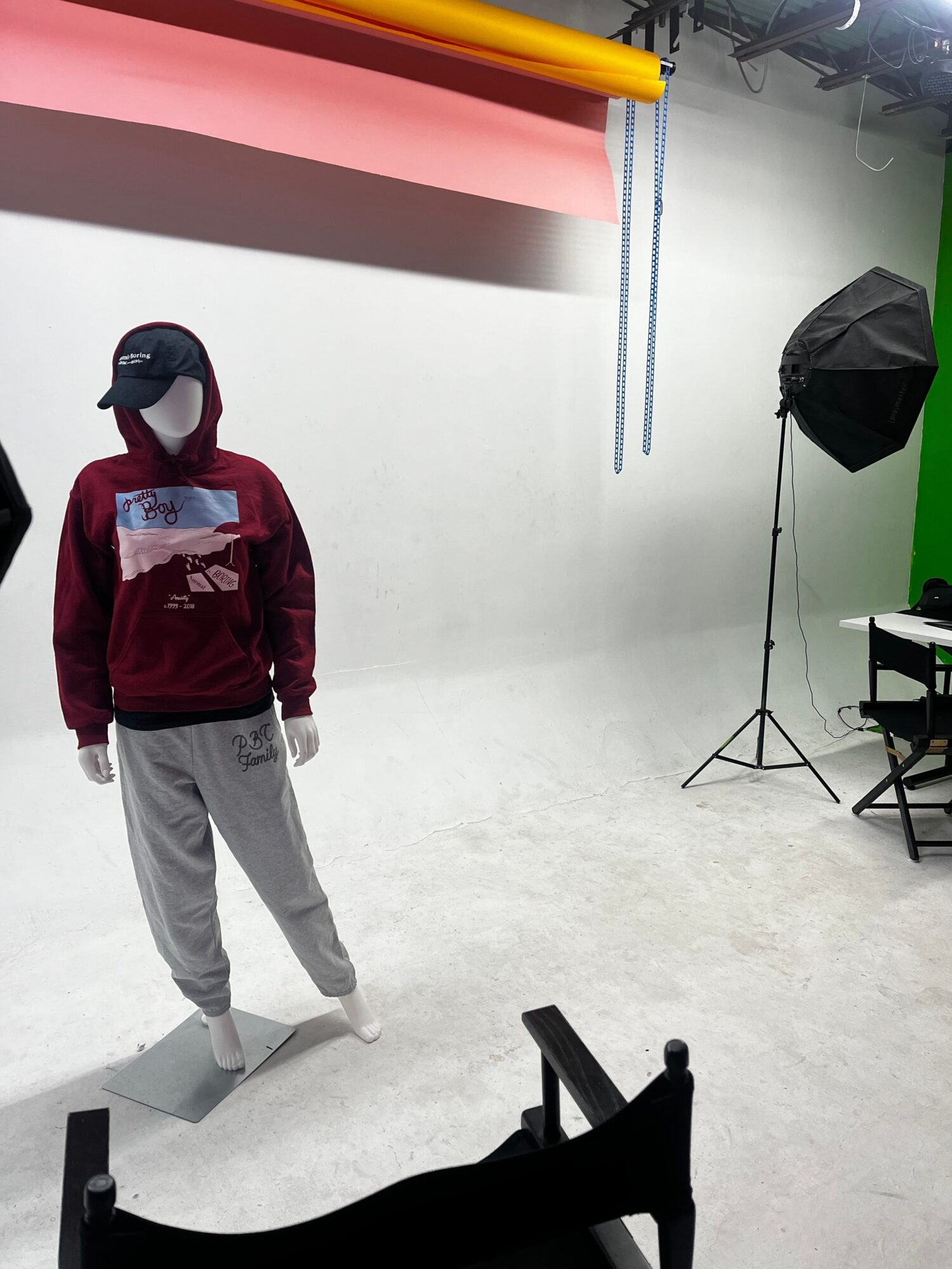 Person in a studio with photography equipment, standing on a white floor, wearing a red jacket and gray pants.