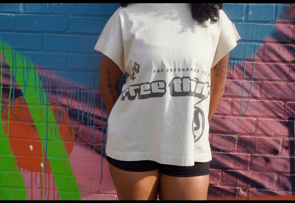 Person standing in front of a colorful graffiti wall, wearing a white T-shirt and black shorts, with curly hair visible.