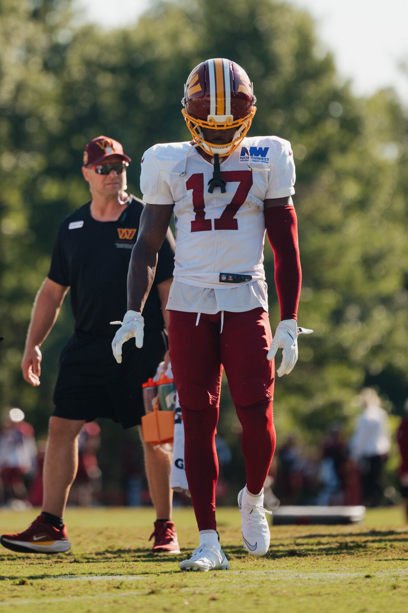 Football player wearing jersey number 17 walking on field with referee nearby, trees in background.