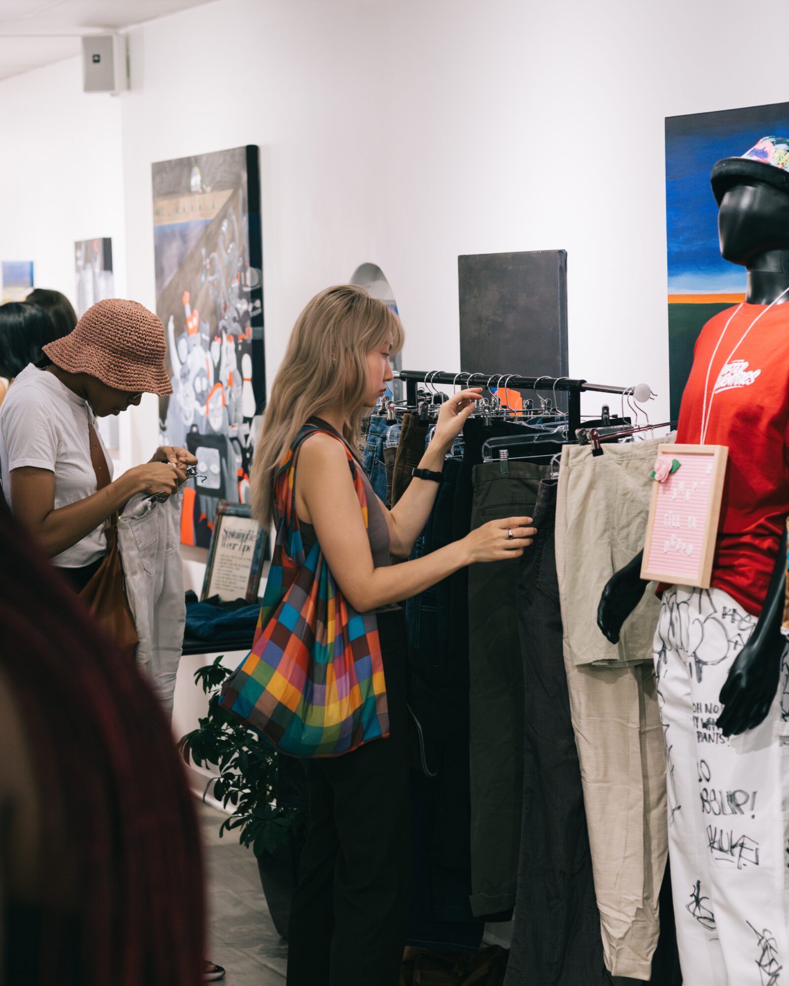 People shopping in a store, browsing clothing and accessories, with mannequins and artwork on the walls.