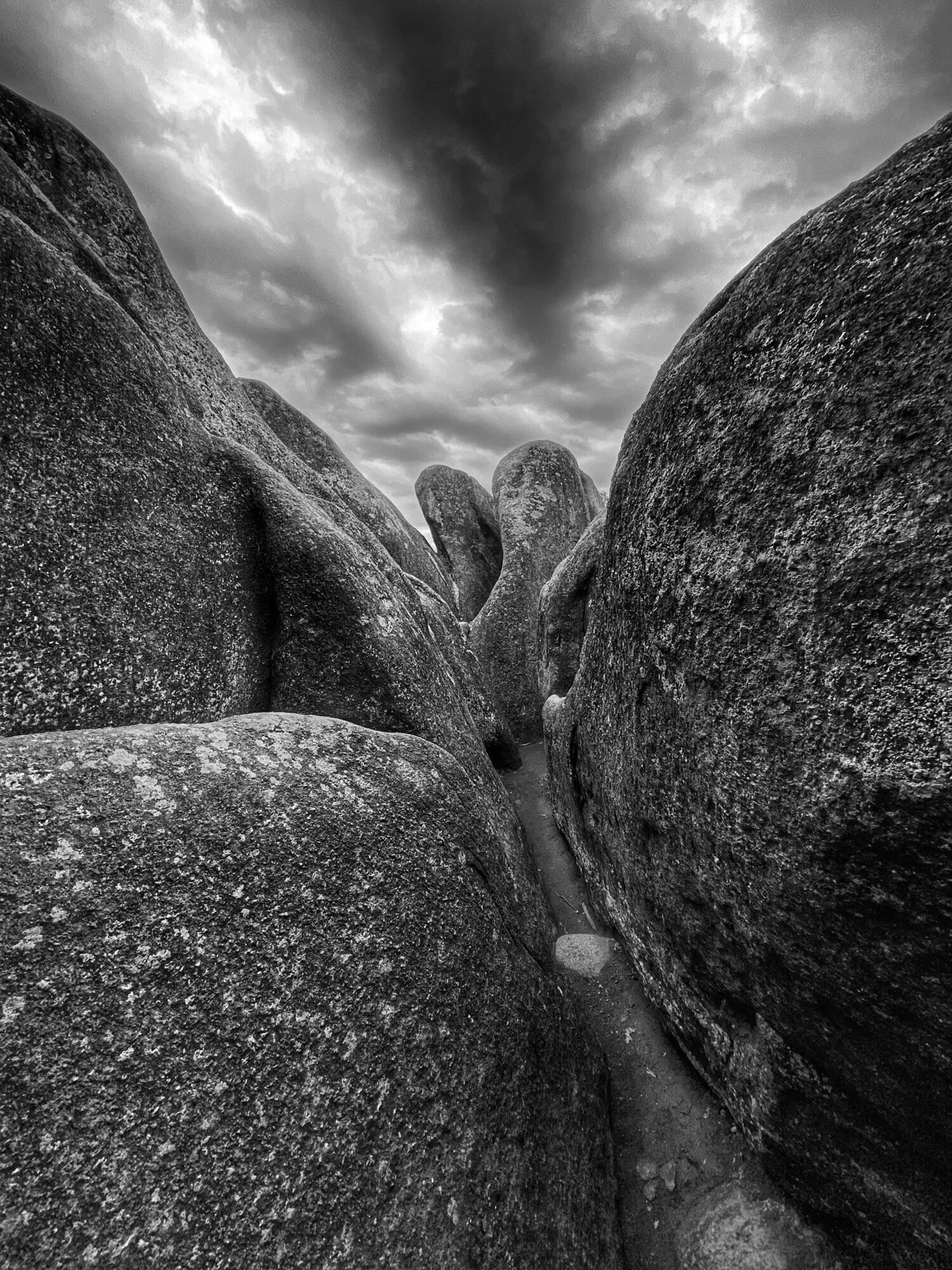 Large rocks with a narrow gap between them, cloudy sky above, in black and white.