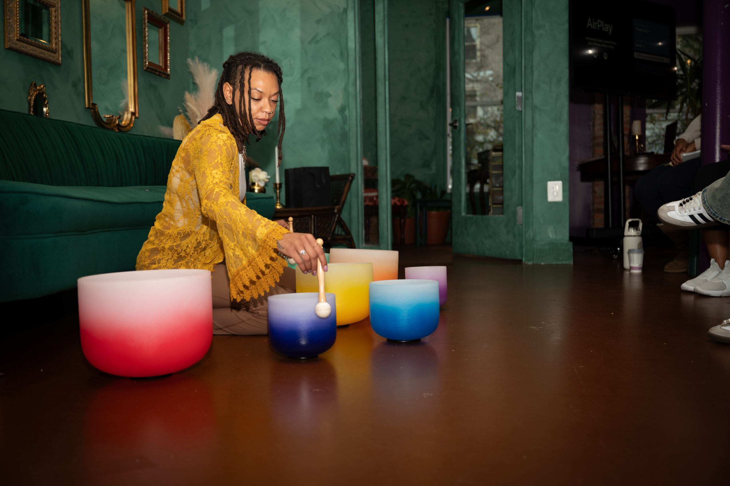 Person in yellow dress arranging colorful candles on a table in a room with green walls and artwork.