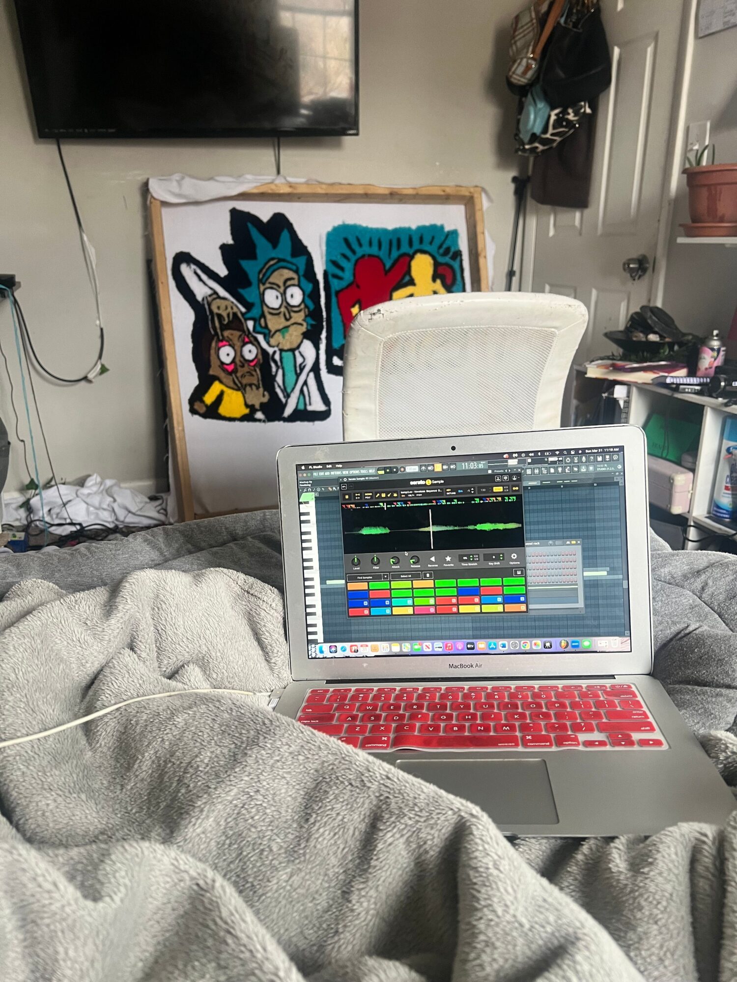 Person using a laptop with a music editing program open, sitting on a couch in a room with artwork and a TV.