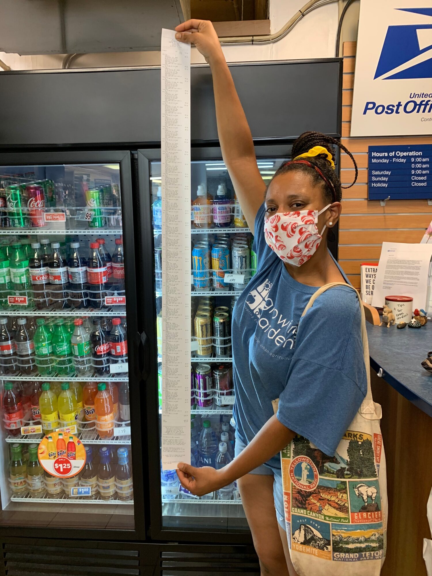 Girl wearing a face mask and a blue shirt, reaching for a drink in a refrigerator, with posters and items behind her.