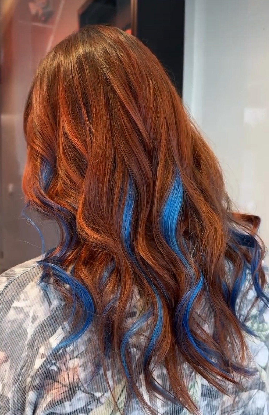Back view of long, wavy hair with reddish-brown and blue streaks, styled in loose curls.