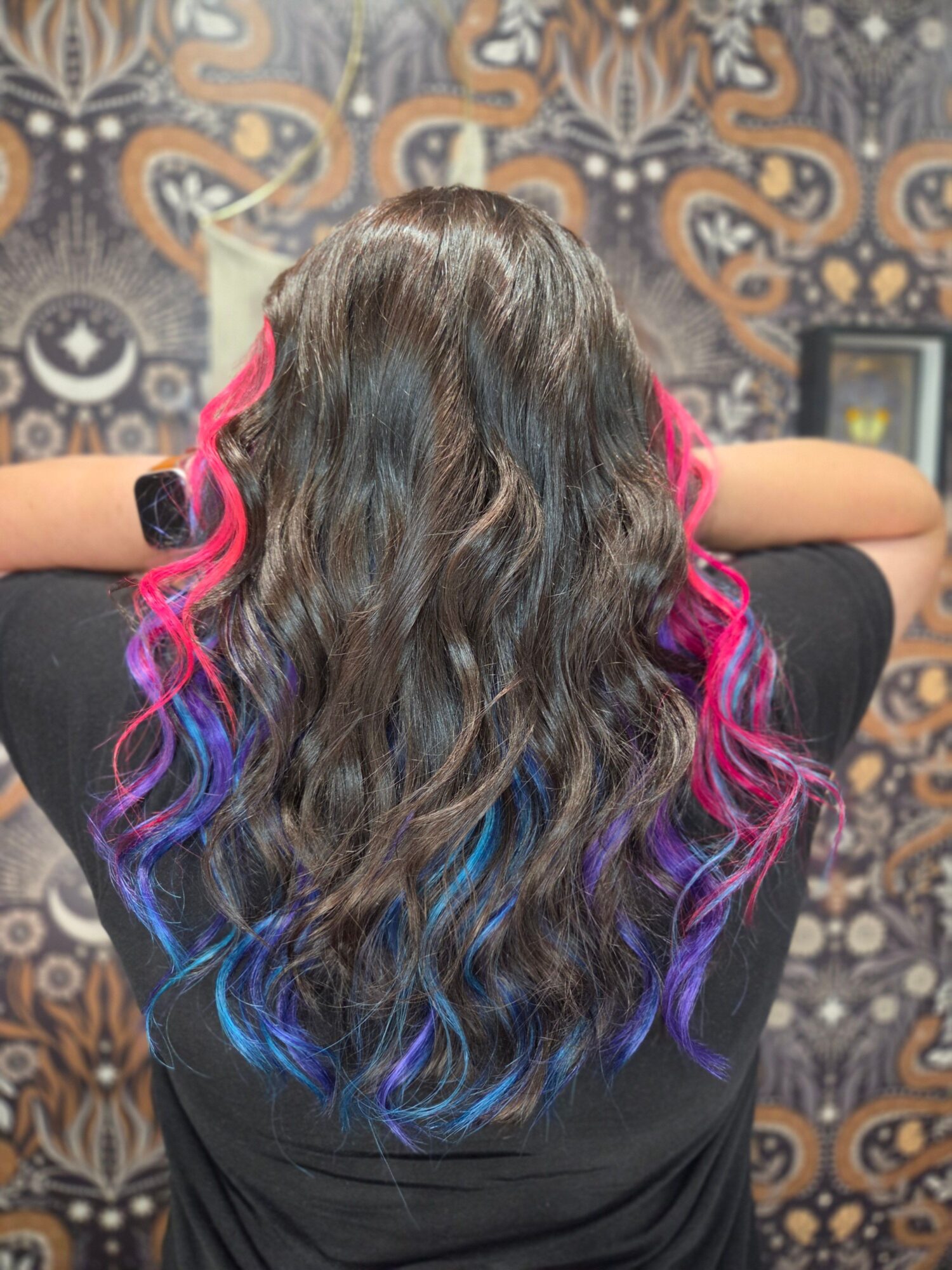 Person with long, wavy hair dyed pink, purple, and blue, lying on a patterned surface, viewed from above.