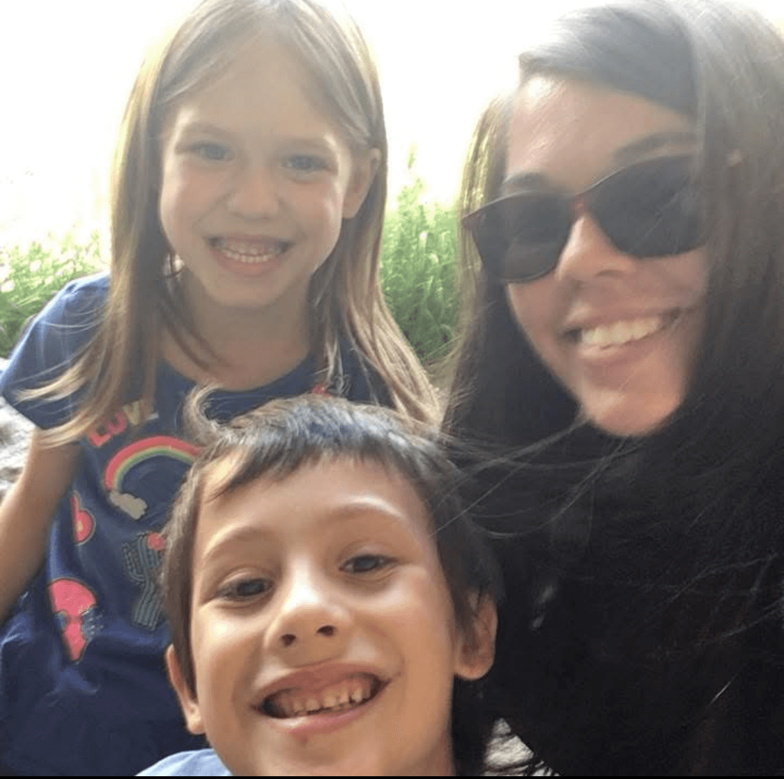 Two adults and a child smile for a close-up photo outdoors.