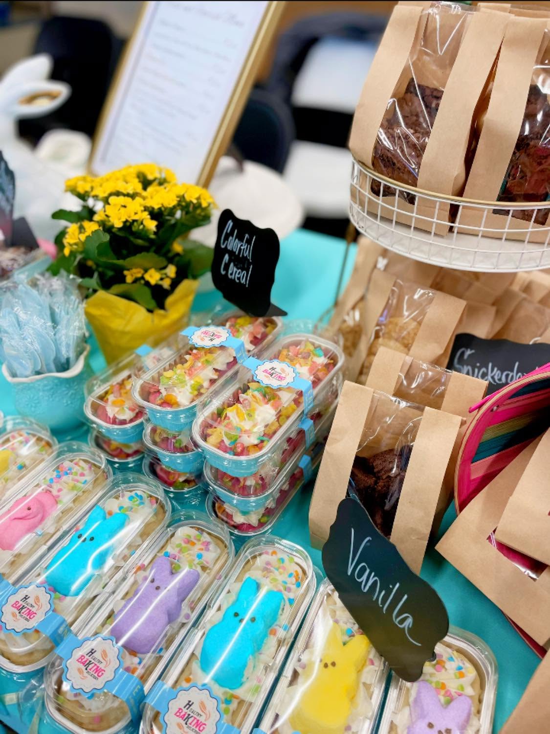Display of colorful decorated cupcakes, flowers, and paper bags on a table at an event.