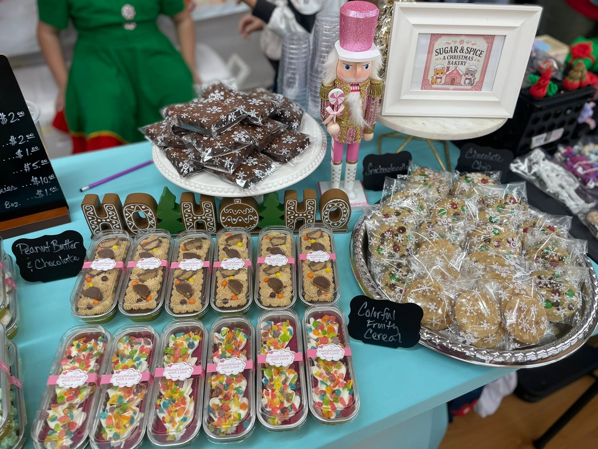 Display of decorated cookies and treats on a table, with a pink nutcracker figure and framed sign in the background.