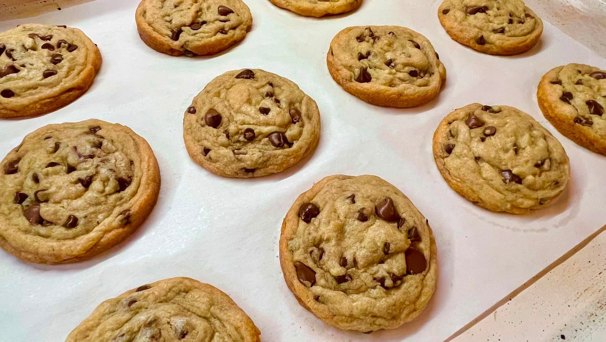 Several chocolate chip cookies on a white surface, some overlapping, with a golden-brown color and visible chocolate chips.
