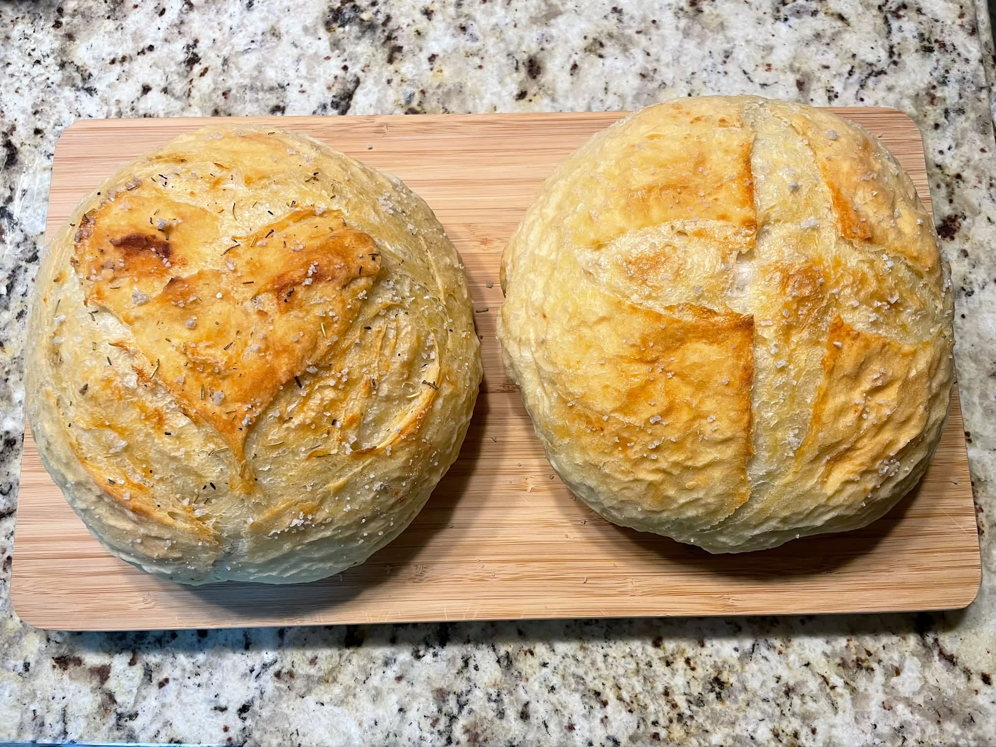 Two round bread rolls on a wooden board, placed on a speckled granite countertop.