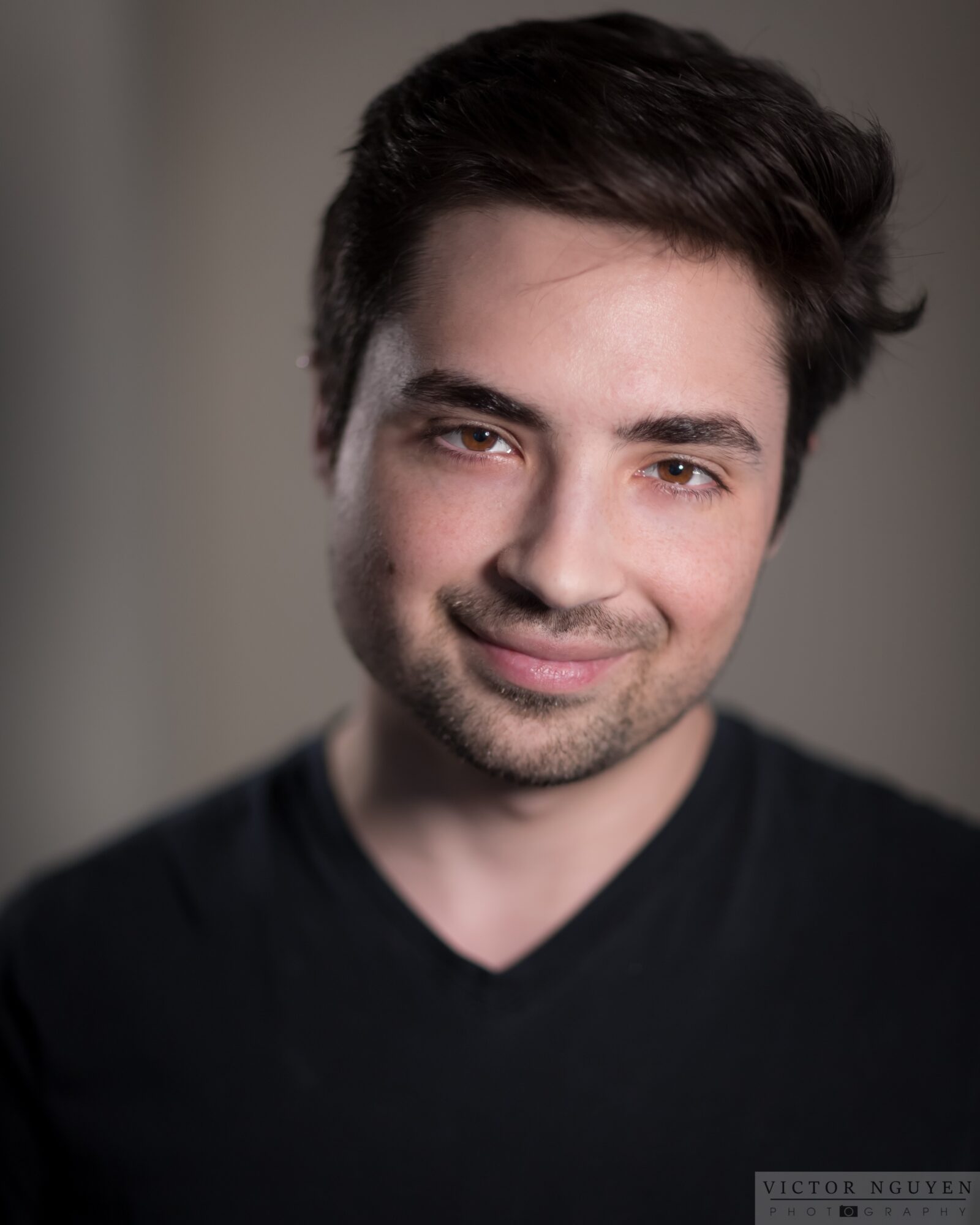 Young man with dark hair and a slight smile, wearing a black V-neck shirt, facing forward.
