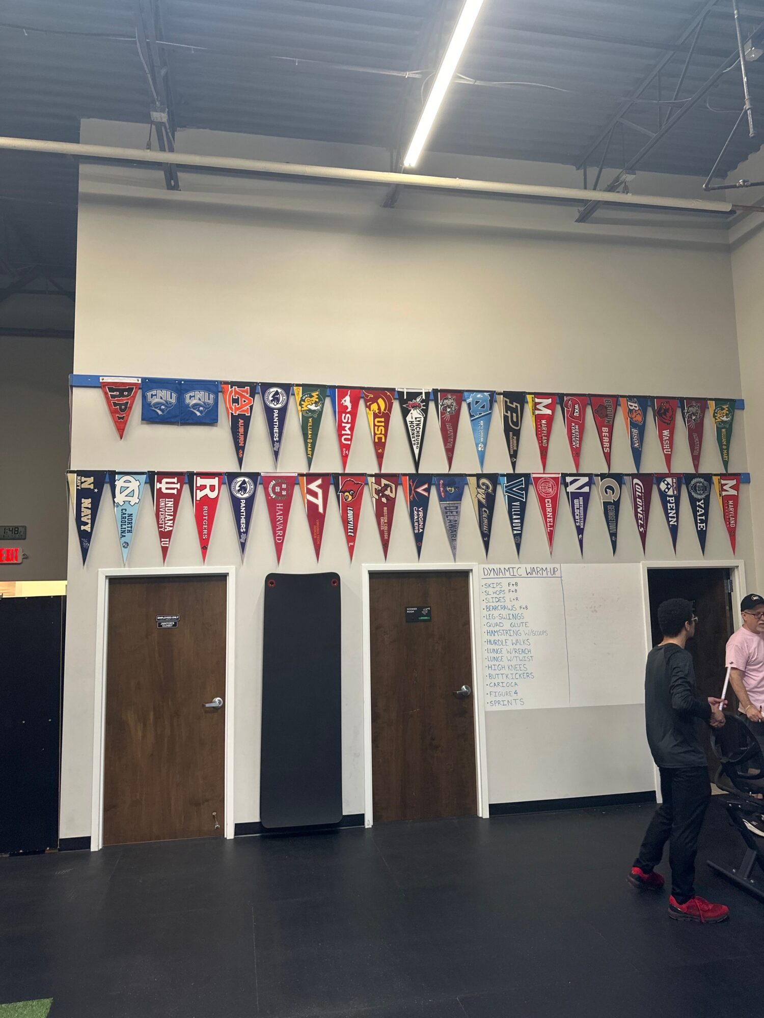 Display of various college pennants on a wall, with people in a room, some standing near a whiteboard.