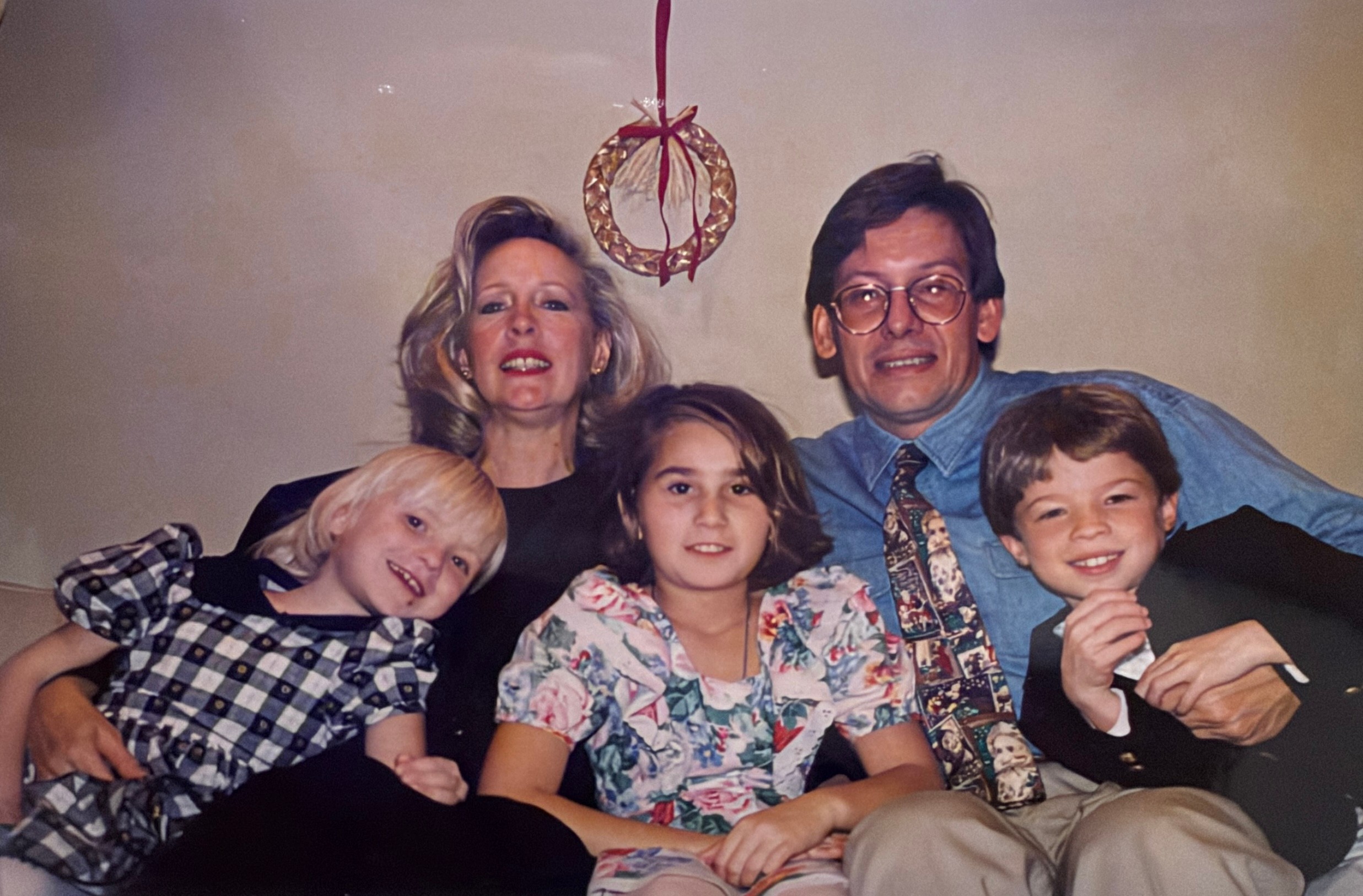 Four people sitting together, two adults and two children, smiling, with a decorative hanging ornament above them.