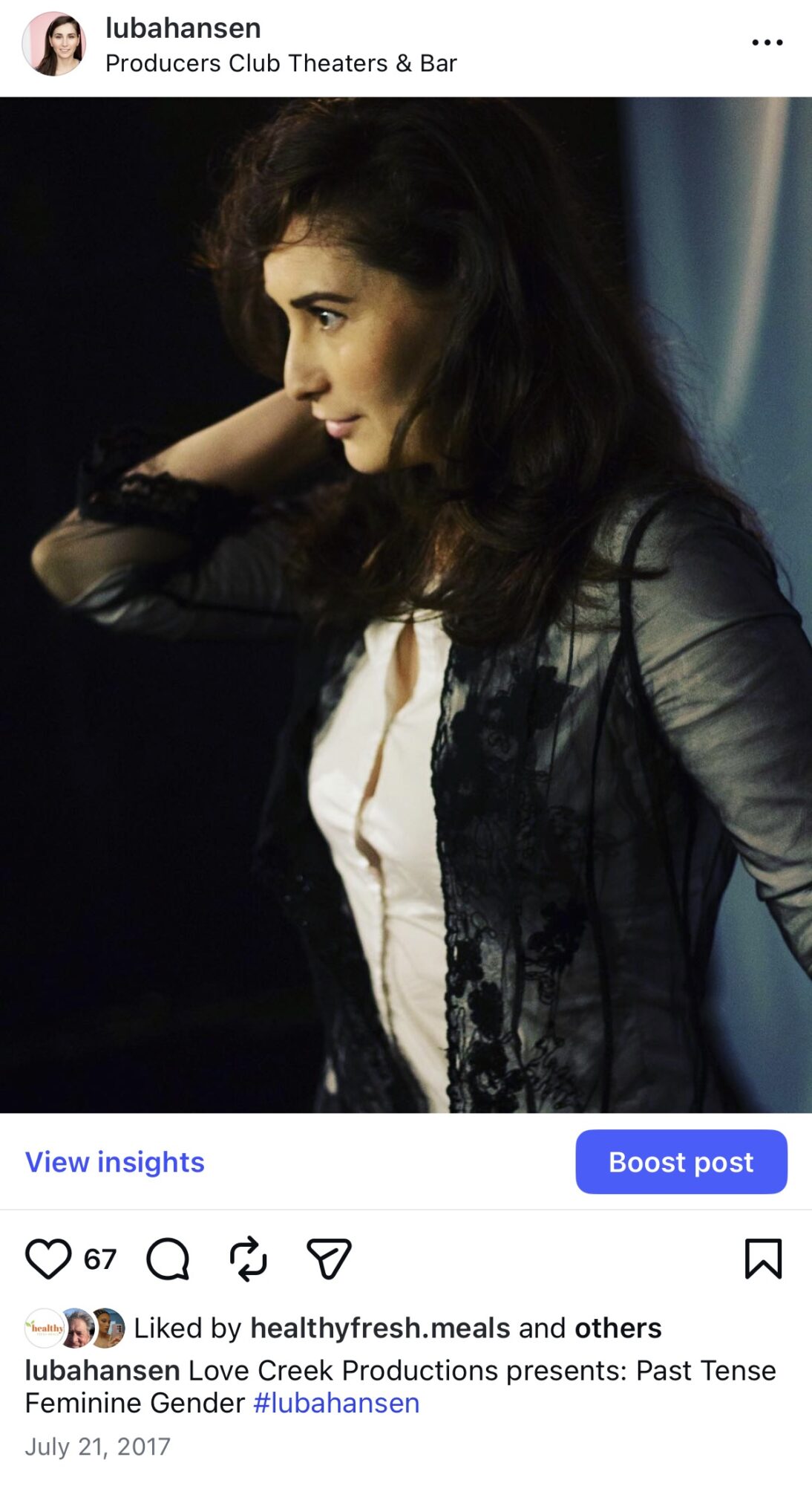 Side profile of a woman with dark hair, wearing a black and white outfit, looking to the side against a dark background.