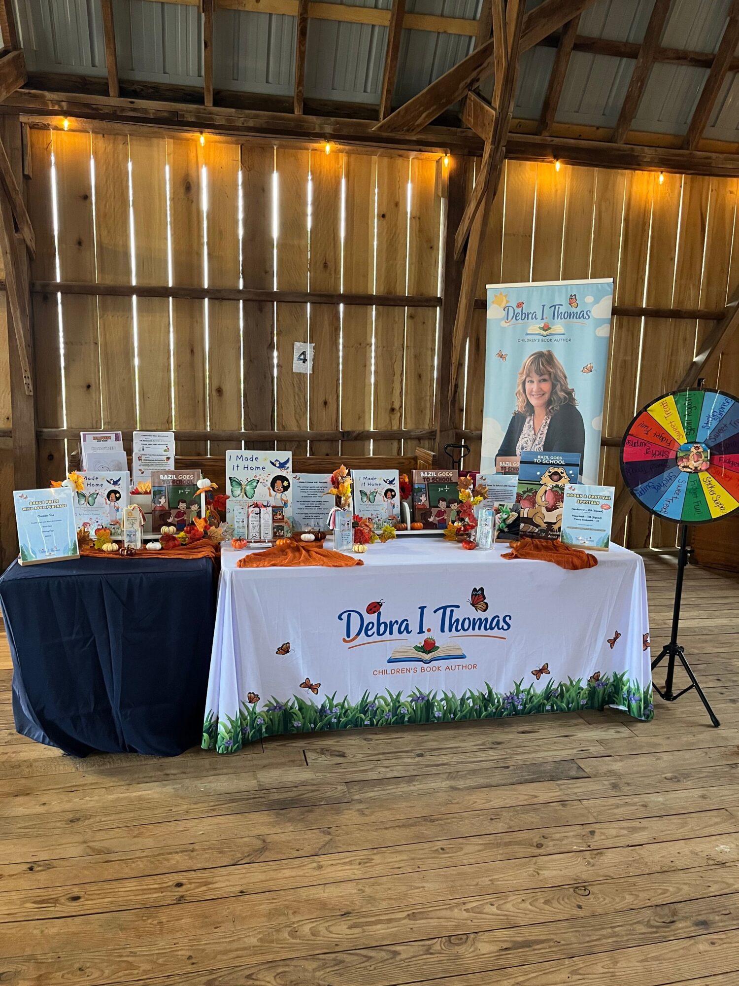 Table with a Dream Foundation banner, various items, and a colorful spinning wheel in a wooden barn setting.