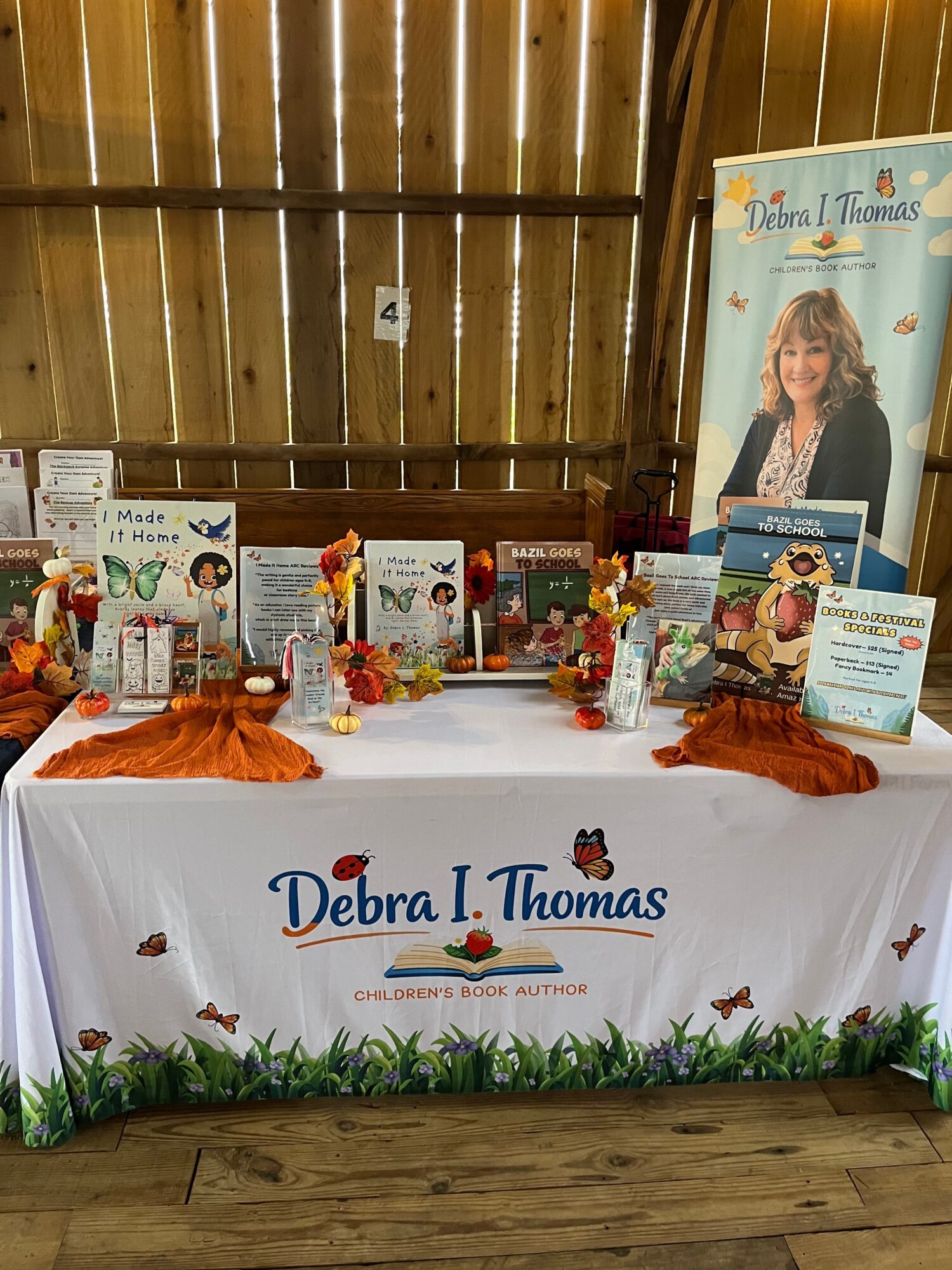 Display table with books, decorations, and a banner reading 'Debra L. Thomas' in a wooden-fenced room.