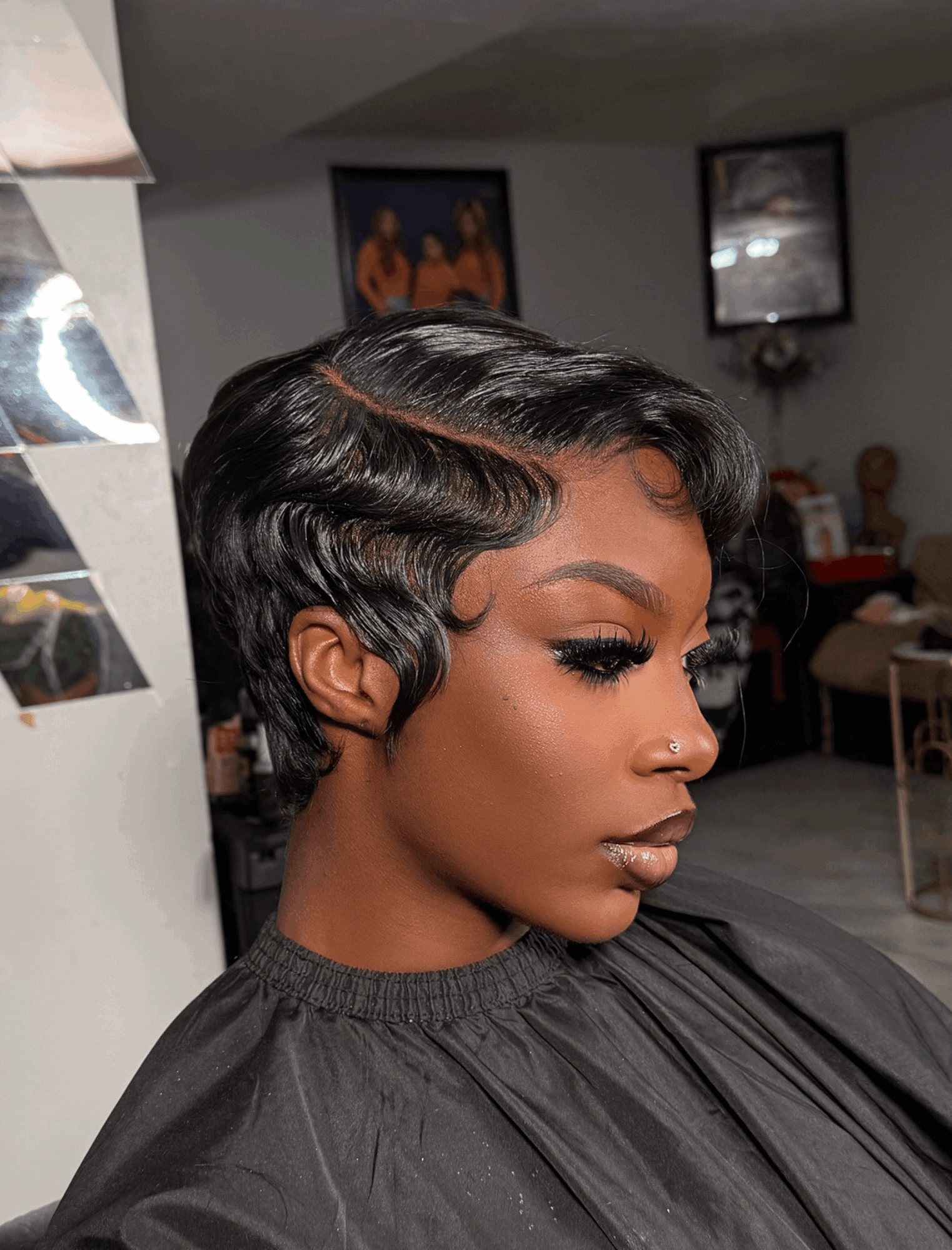 Side profile of a woman with short, wavy black hair and makeup, in a salon setting.