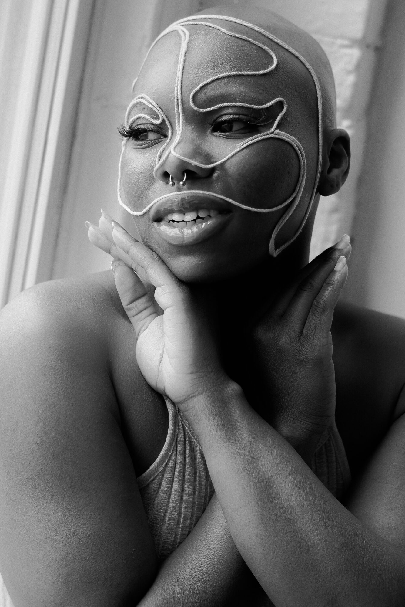 Woman with artistic face makeup and wire design, touching her face near her chin, in black and white.