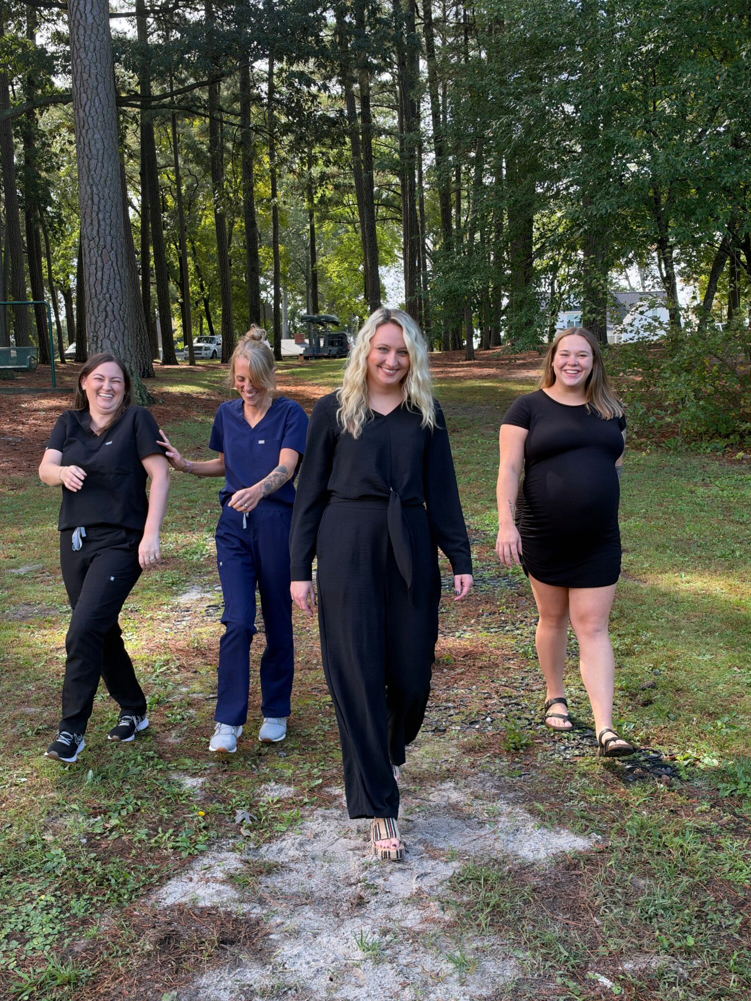 Four people stand together on a wooded path among tall trees.