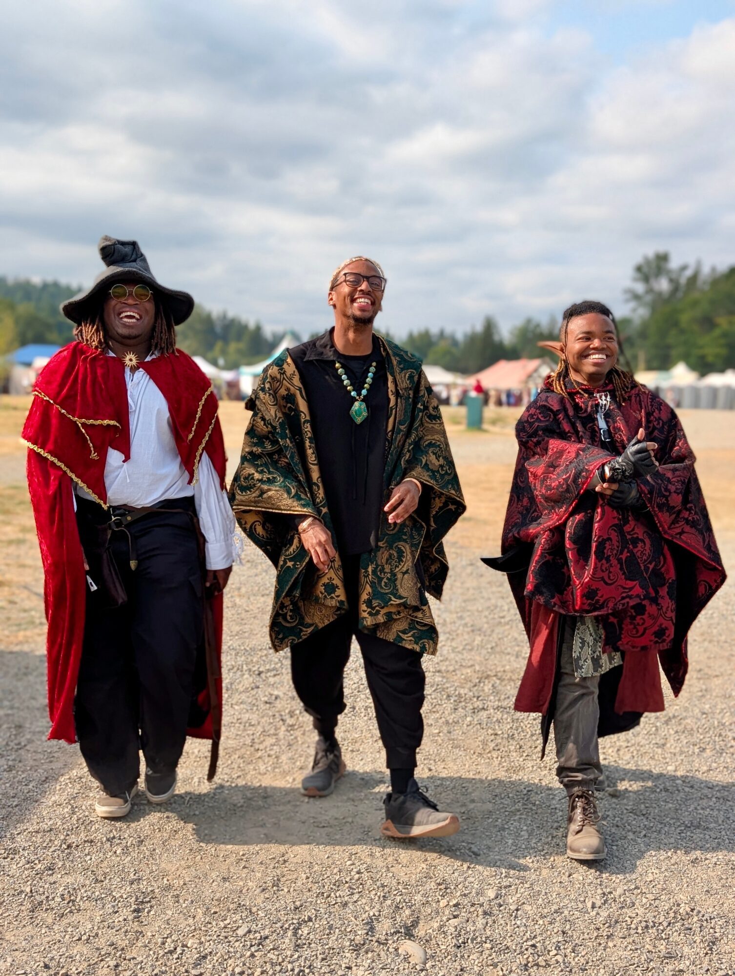 Three people in colorful layered clothing walk across a gravel area beneath a cloudy sky.