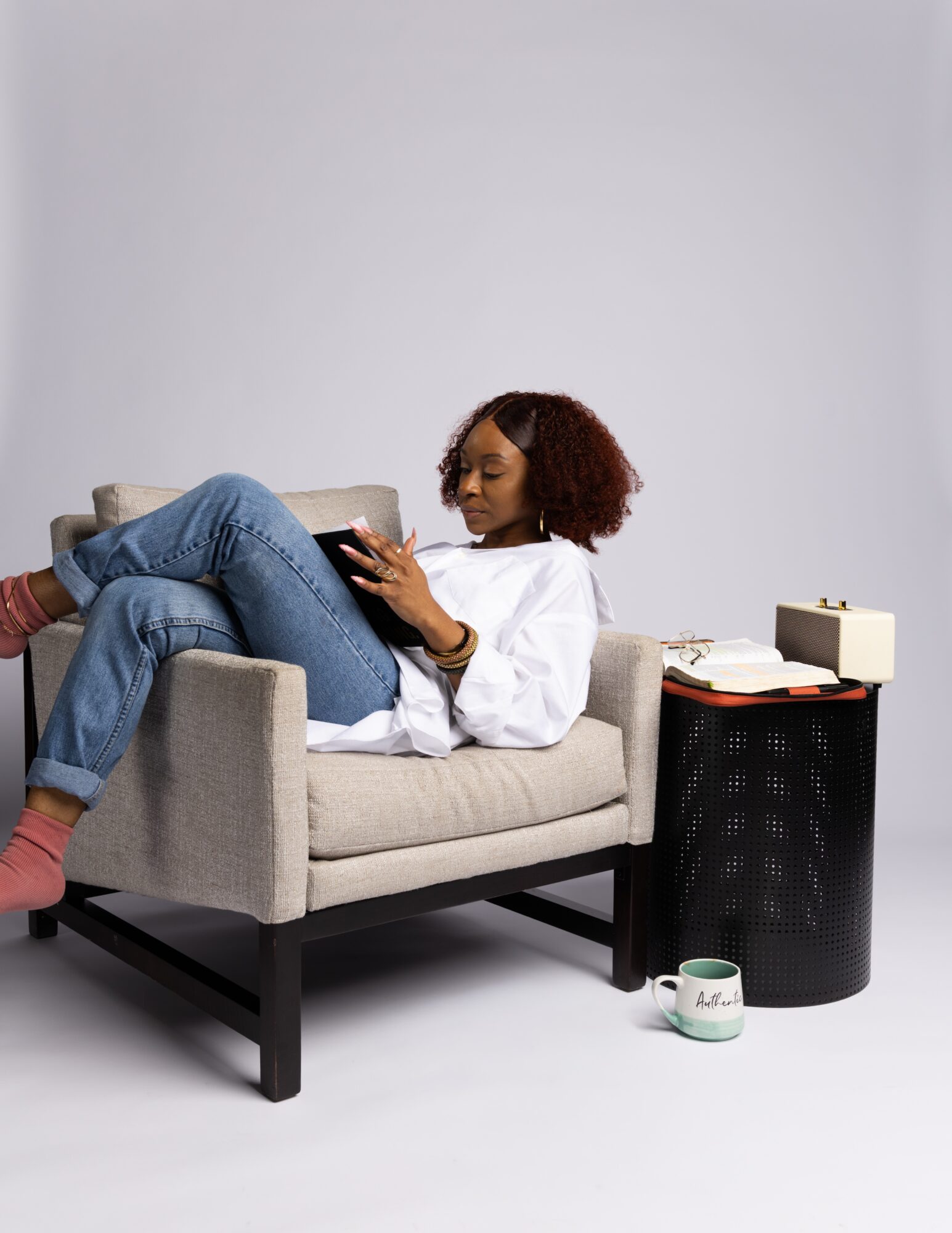 Person reclining in an armchair and reading a book beside a small table.