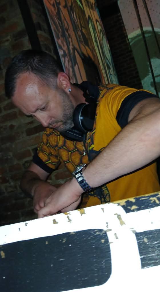 A person in a yellow patterned shirt leans over a painted surface, wearing headphones around the neck.