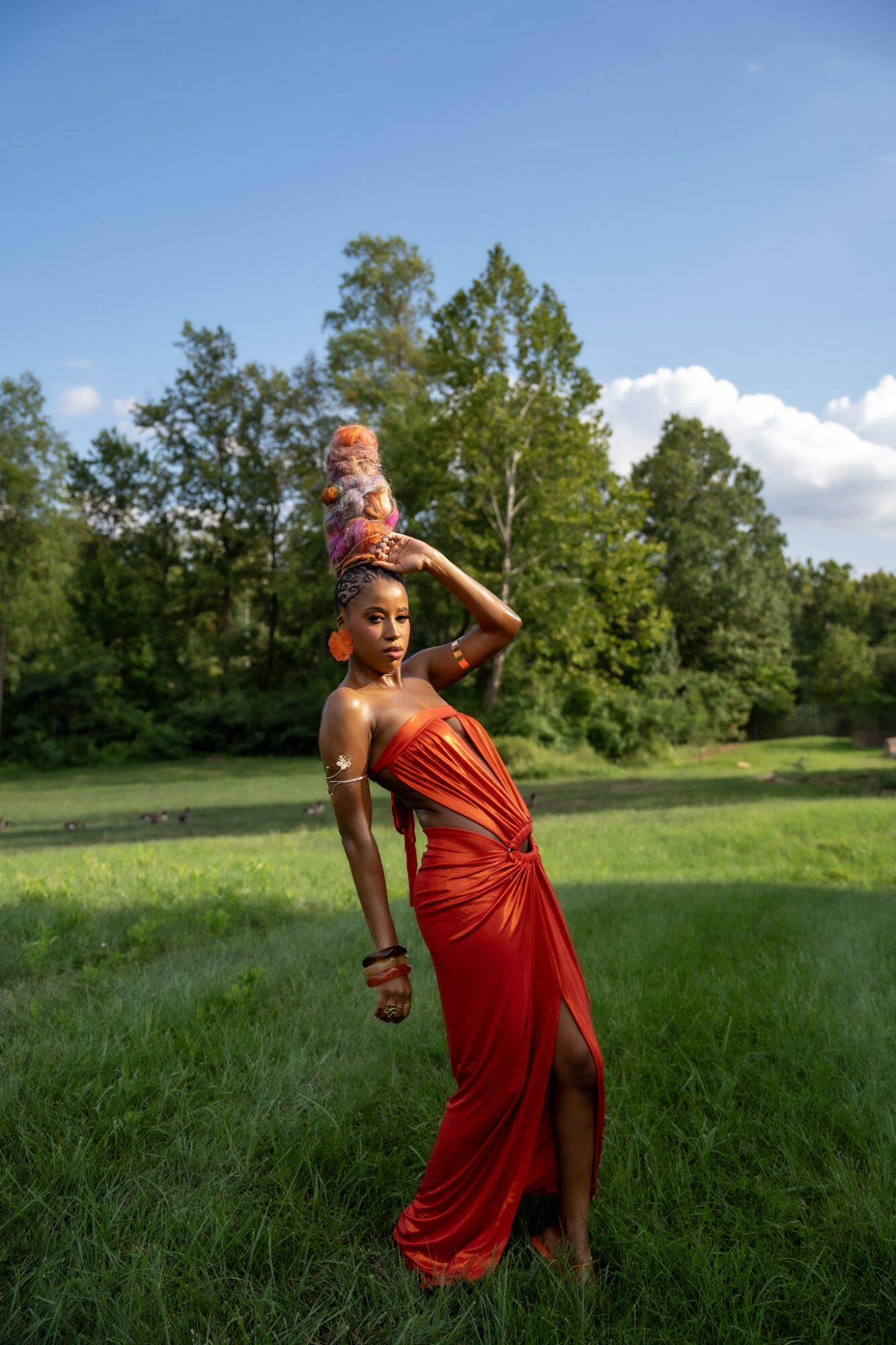 Person in a red draped outfit poses on a grassy field with trees behind them.
