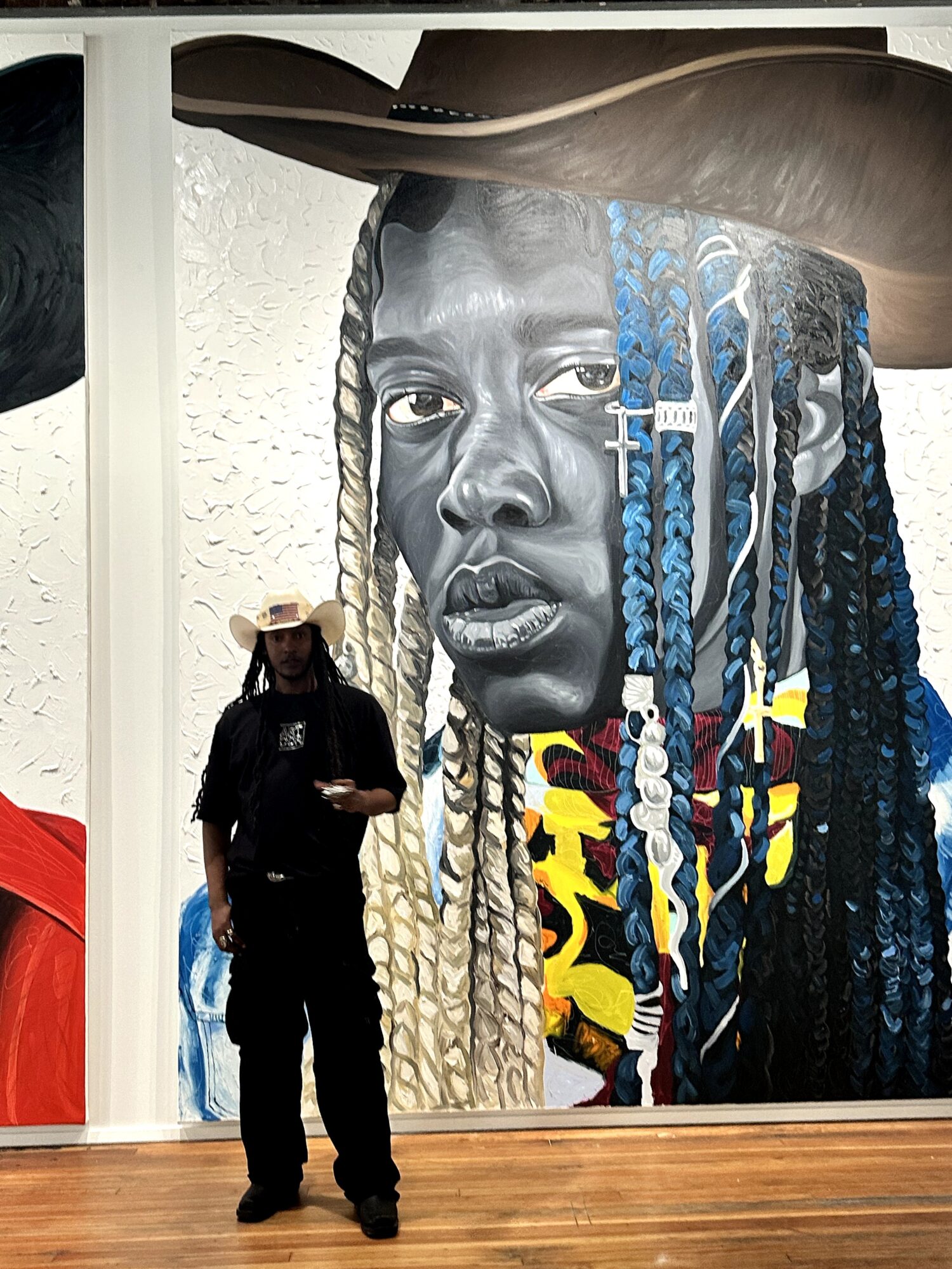 Person standing before a large mural portrait with long braids and colorful details.