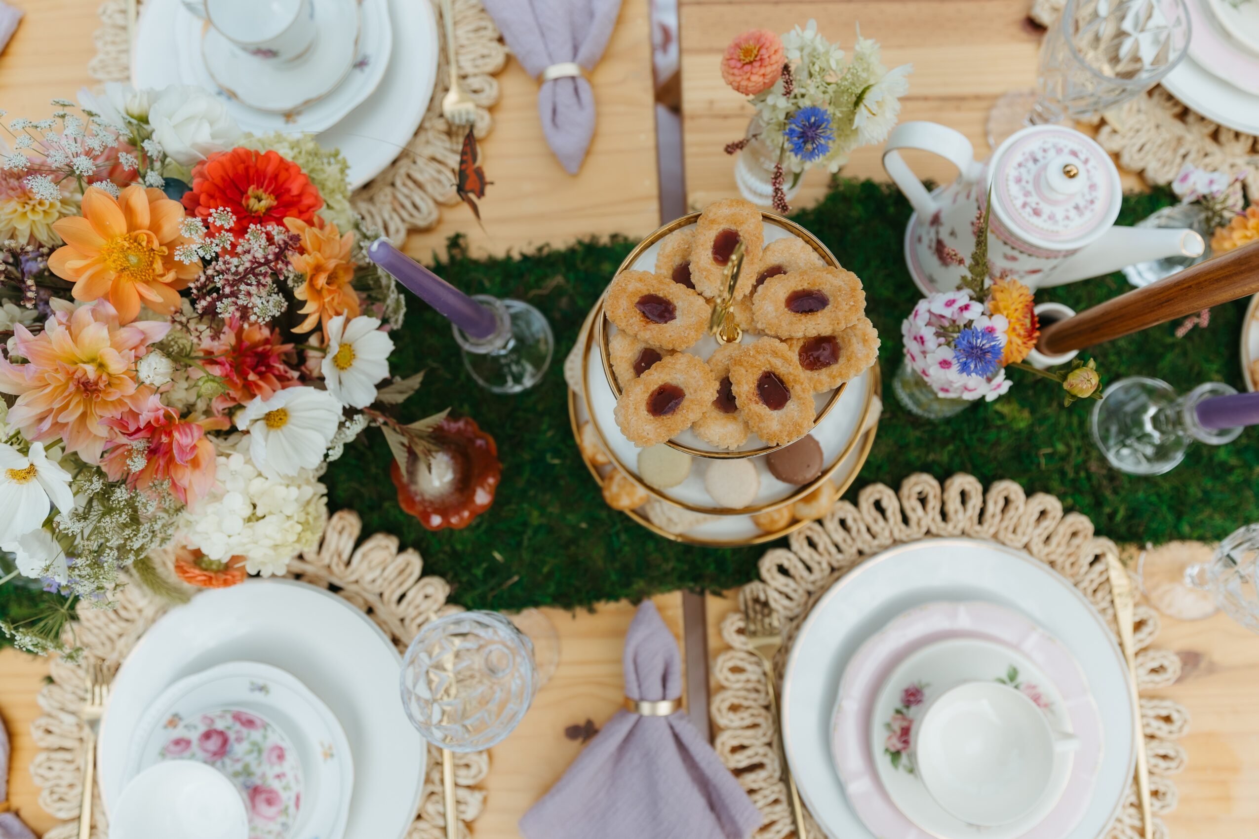 Overhead view of a dining table set with plates, flowers, teacups, pastries, and purple napkins.