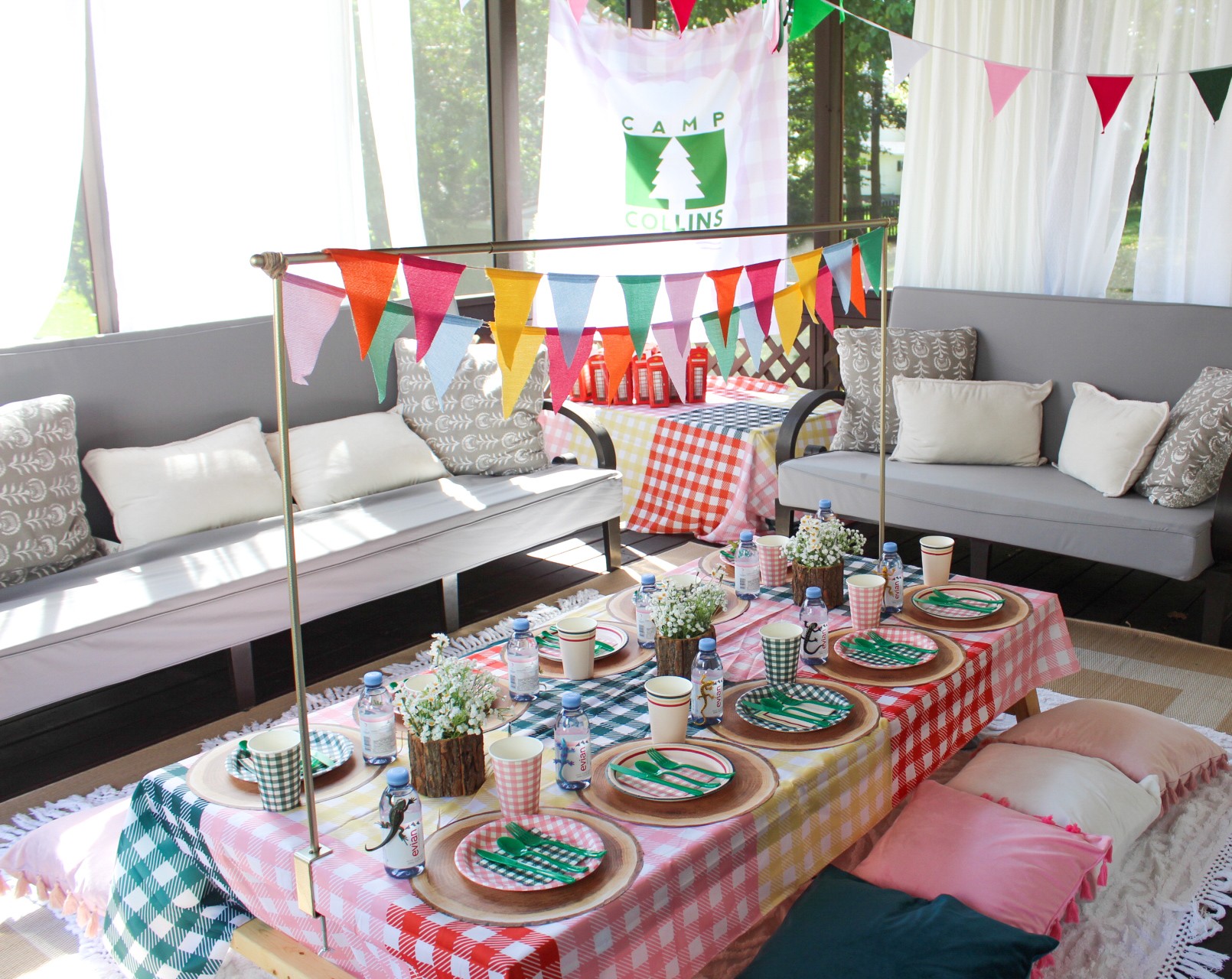 A bright room with sofas, colorful triangular bunting, and a table set with plates, cups, and checkered cloths.