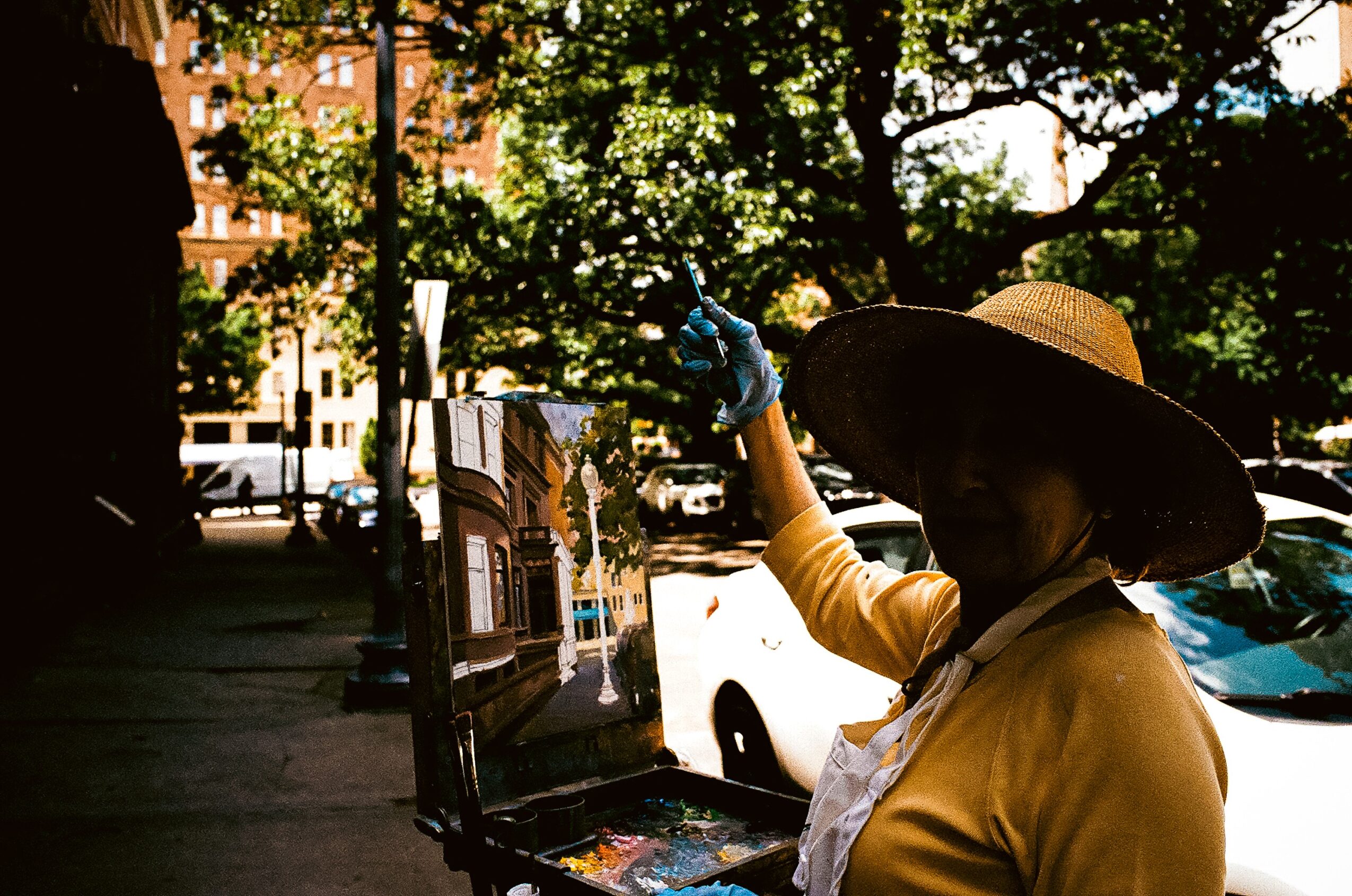 Person wearing a wide-brimmed hat and yellow shirt stands beside a sidewalk cart and parked cars.