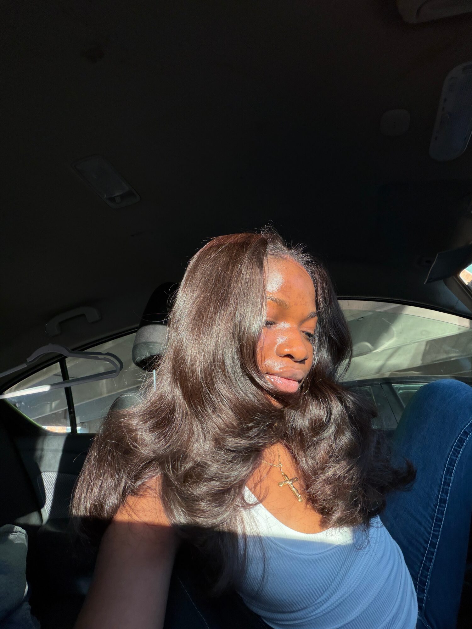 Person with long wavy hair sitting in a car, wearing a light blue top.