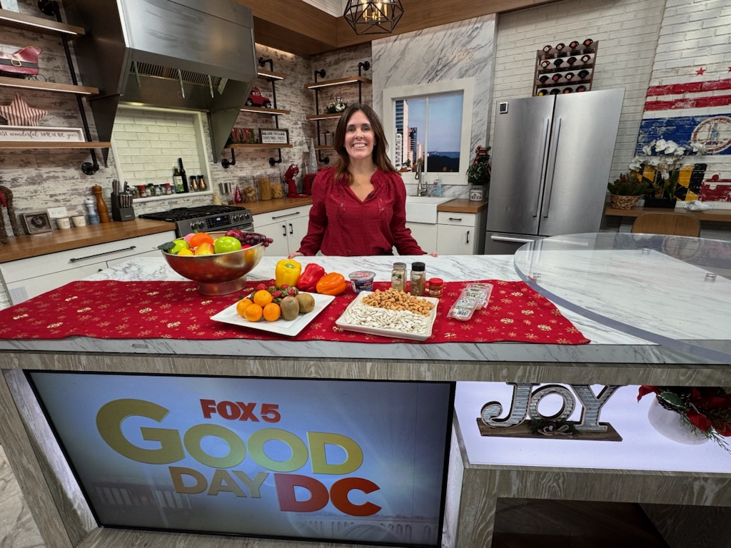 A person stands behind a kitchen counter with fruit, food, and a Fox 5 Good Day DC display below.