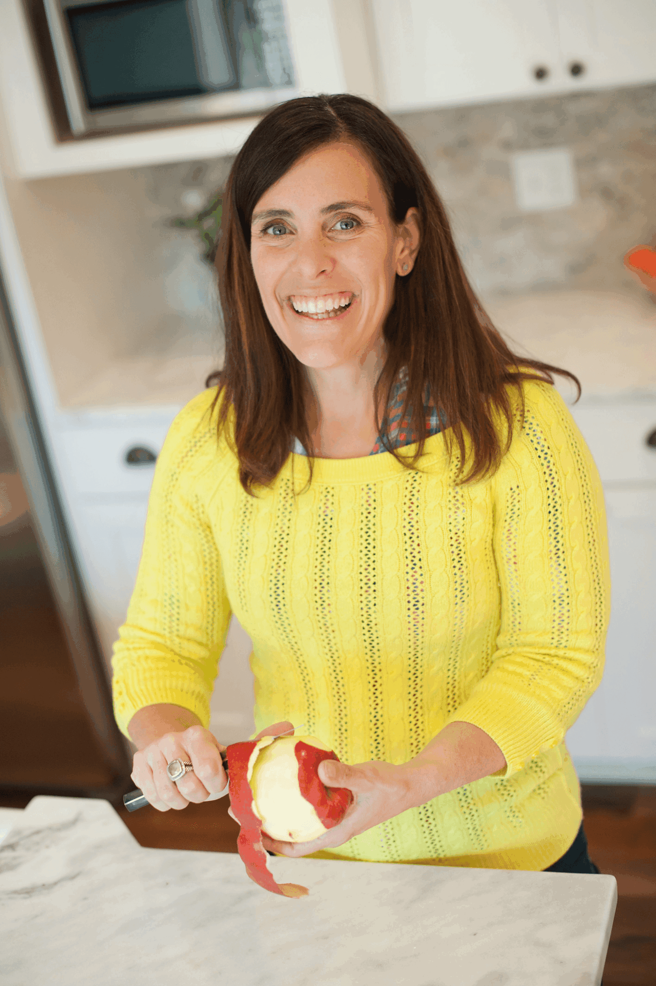 A person in a yellow sweater holds a sliced red apple in a kitchen.