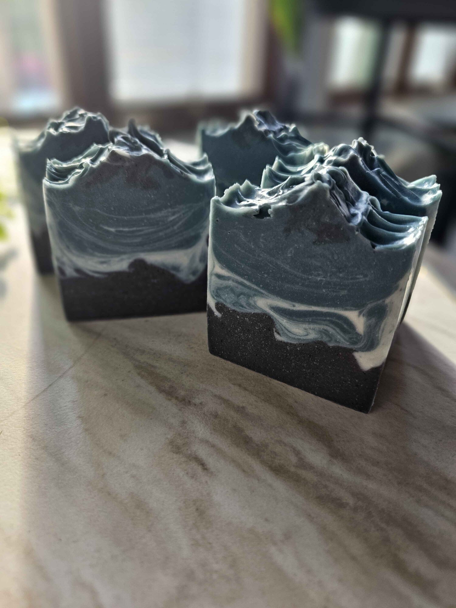 Two dark handmade soap bars with layered gray and white swirls sit on a countertop.