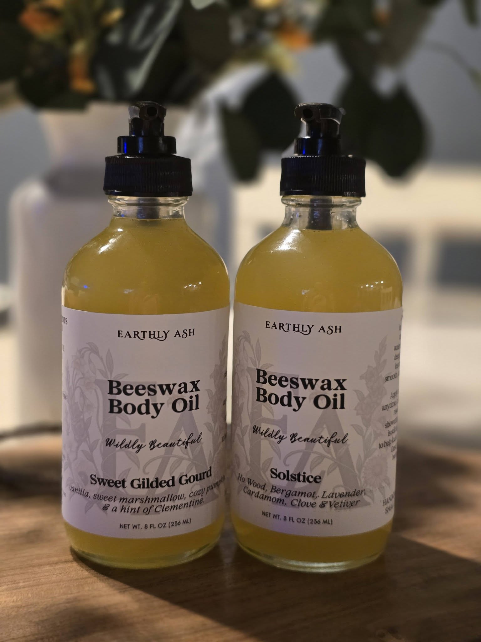 Two amber bottles of Earthly Ash beeswax body oil with black pumps on a wooden counter.