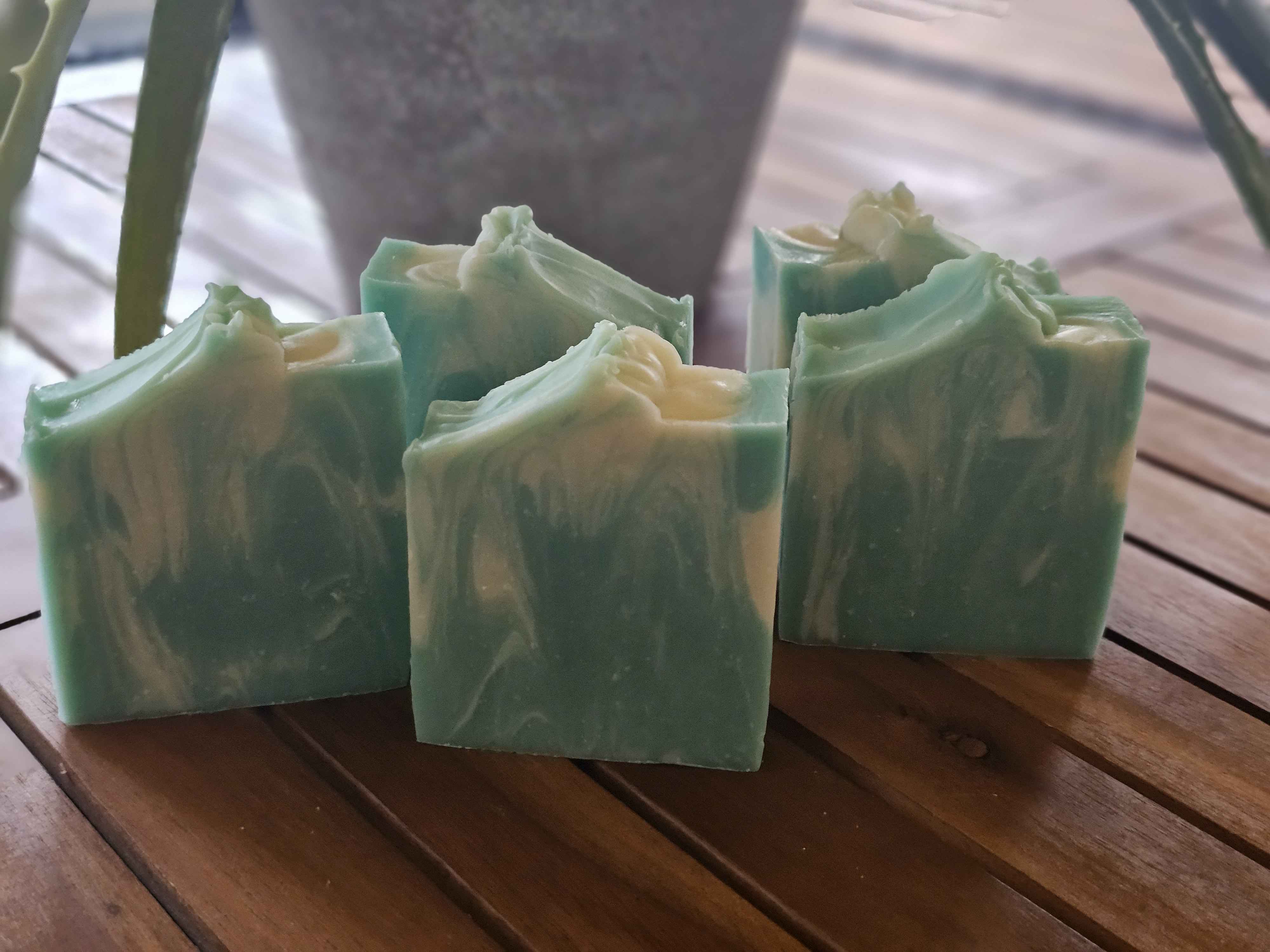 Several green rectangular bars of soap sit on a wooden slatted surface.