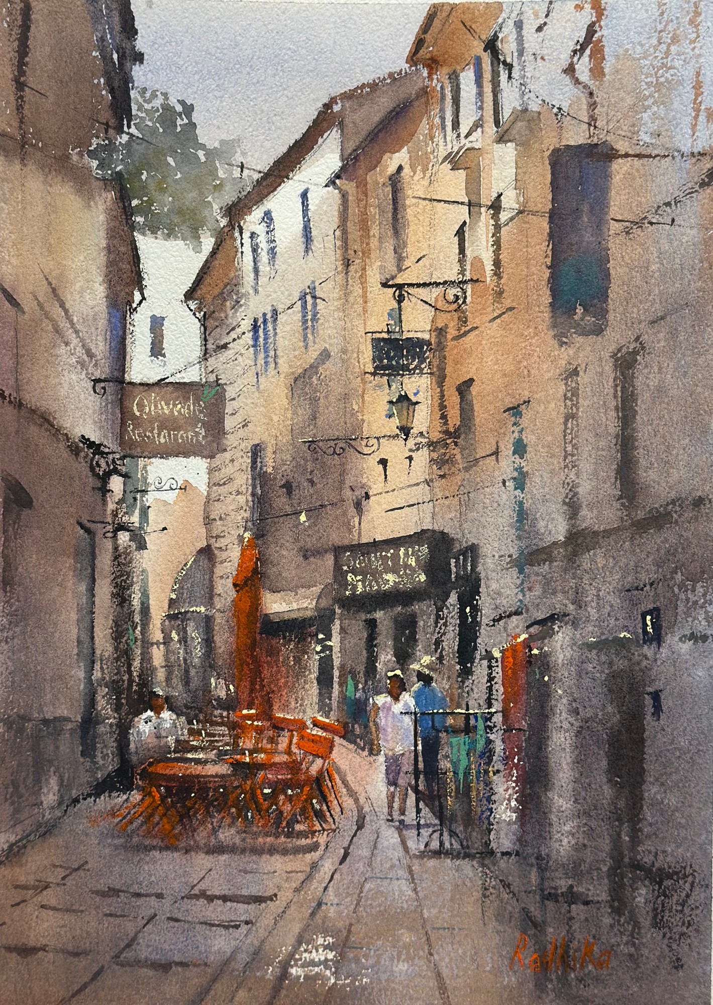 Watercolor street scene with tall buildings, hanging signs, café tables, and people on a narrow sidewalk.